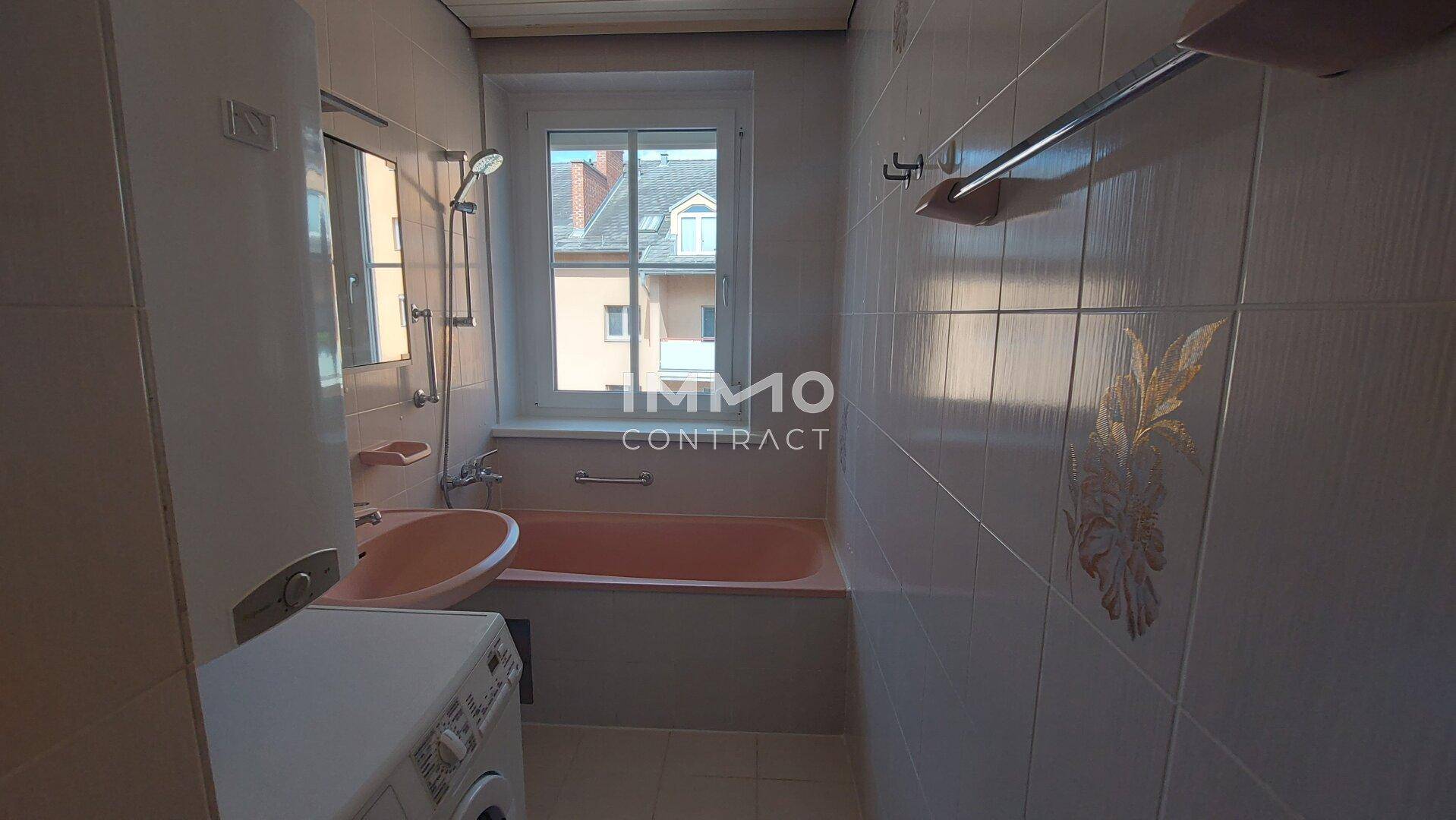 Badezimmer mit rosa Badewanne, passendem Waschbecken, Fliesen und Fenster.