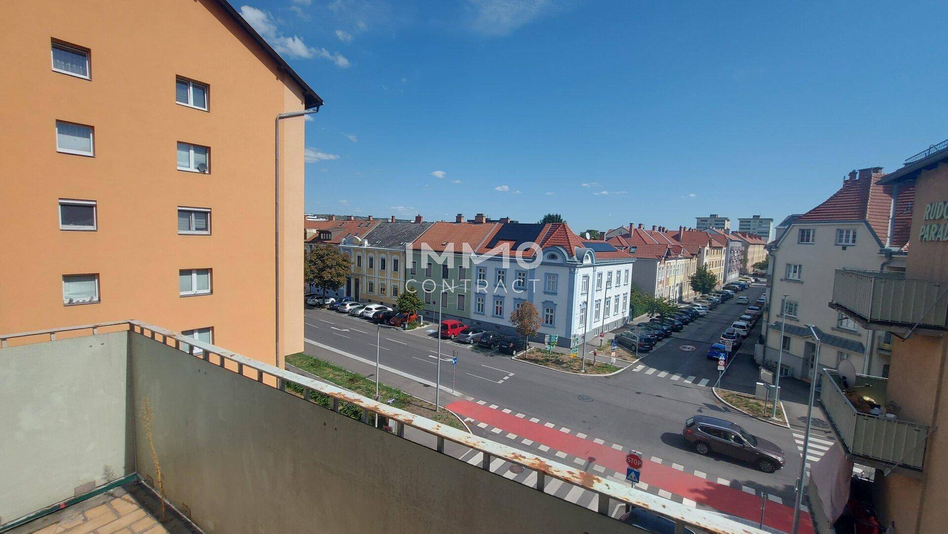 Weitblick von einem Balkon über eine belebte Straße mit städtischer Bebauung.