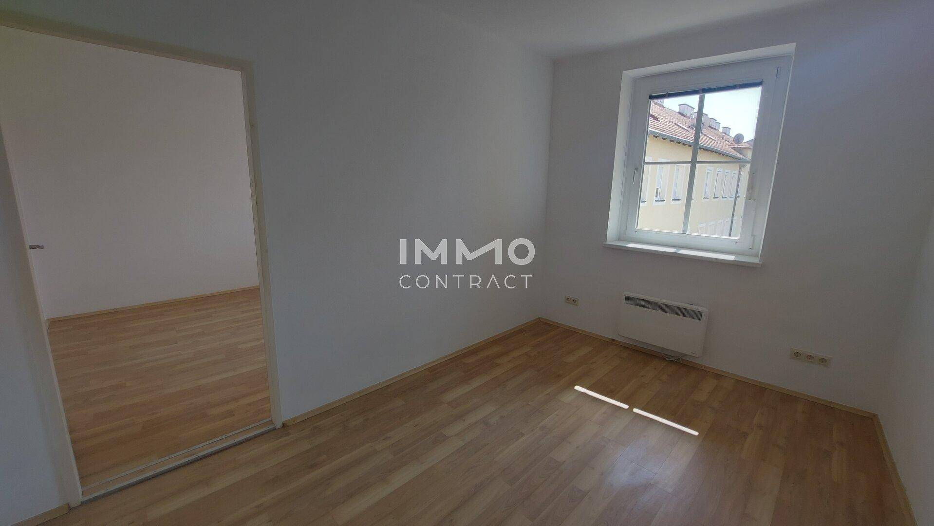 Leeres Zimmer mit Parkettboden, einem Fenster und einem Heizkörper, ideal als Schlafzimmer.