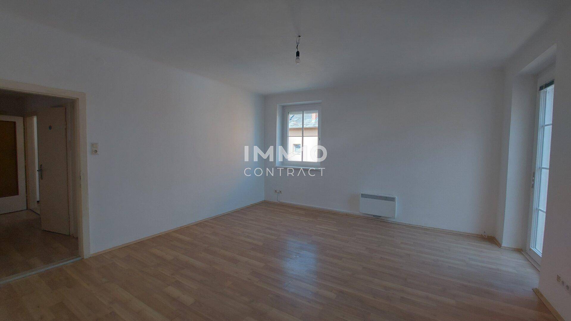 Helles Wohnzimmer mit Parkettboden, weißen Wänden und Zugang zu einem Außenbereich.