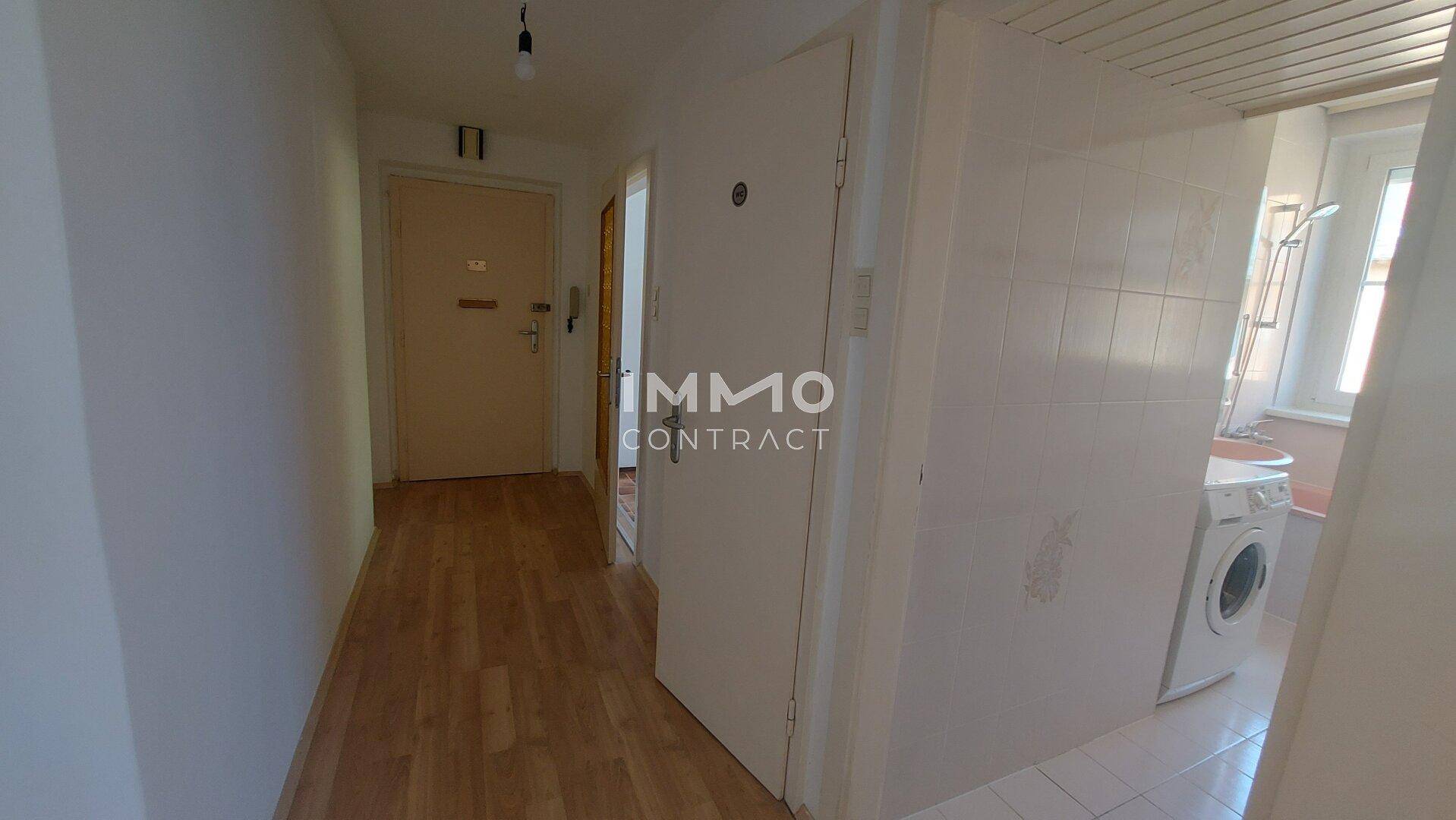 Heller Flur mit Parkettboden, weißen Wänden und Blick in das angrenzende Badezimmer.