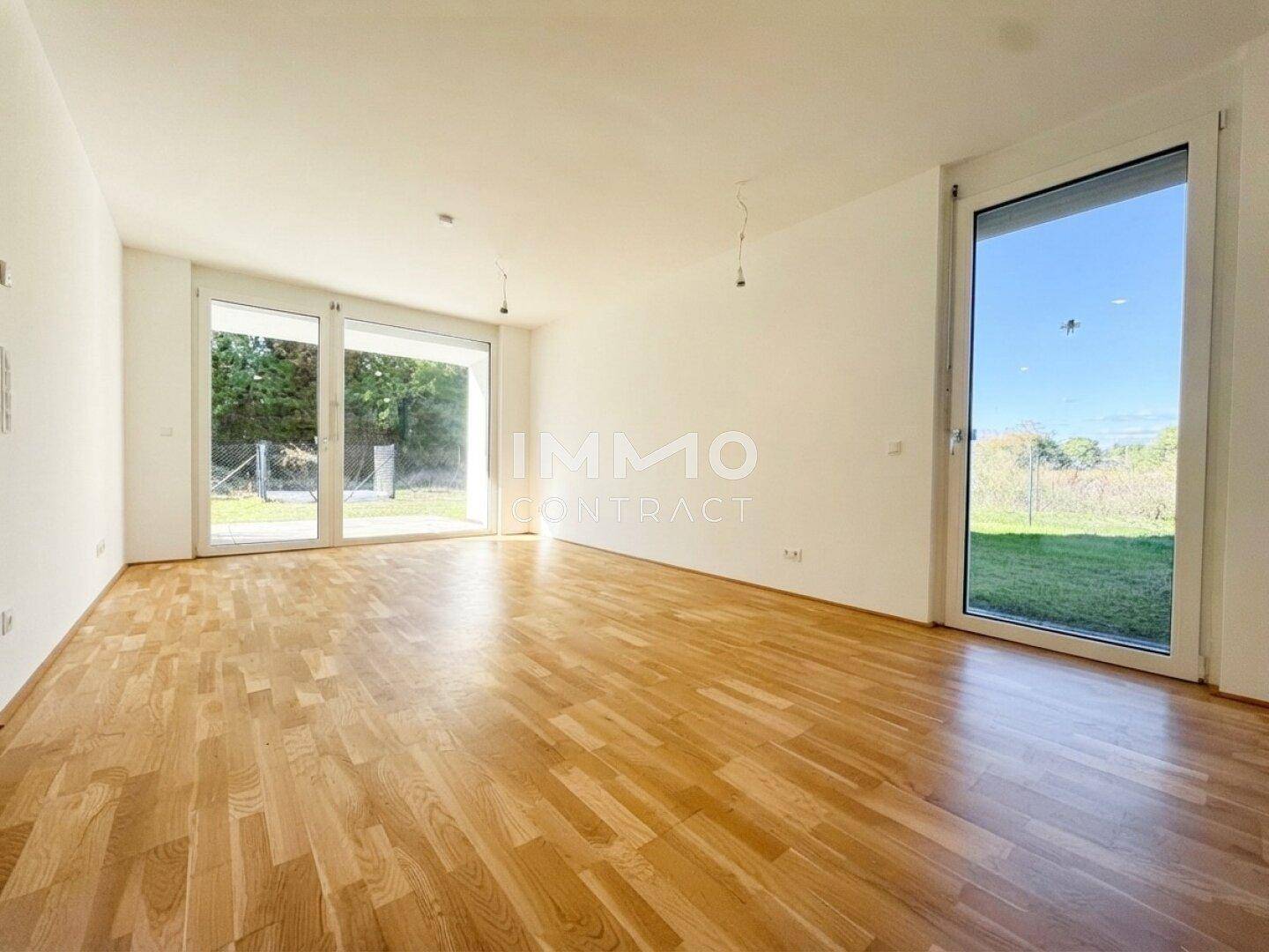 Helles, leeres Wohnzimmer mit Eichenparkettboden und Zugang zum Garten durch große Fenster.