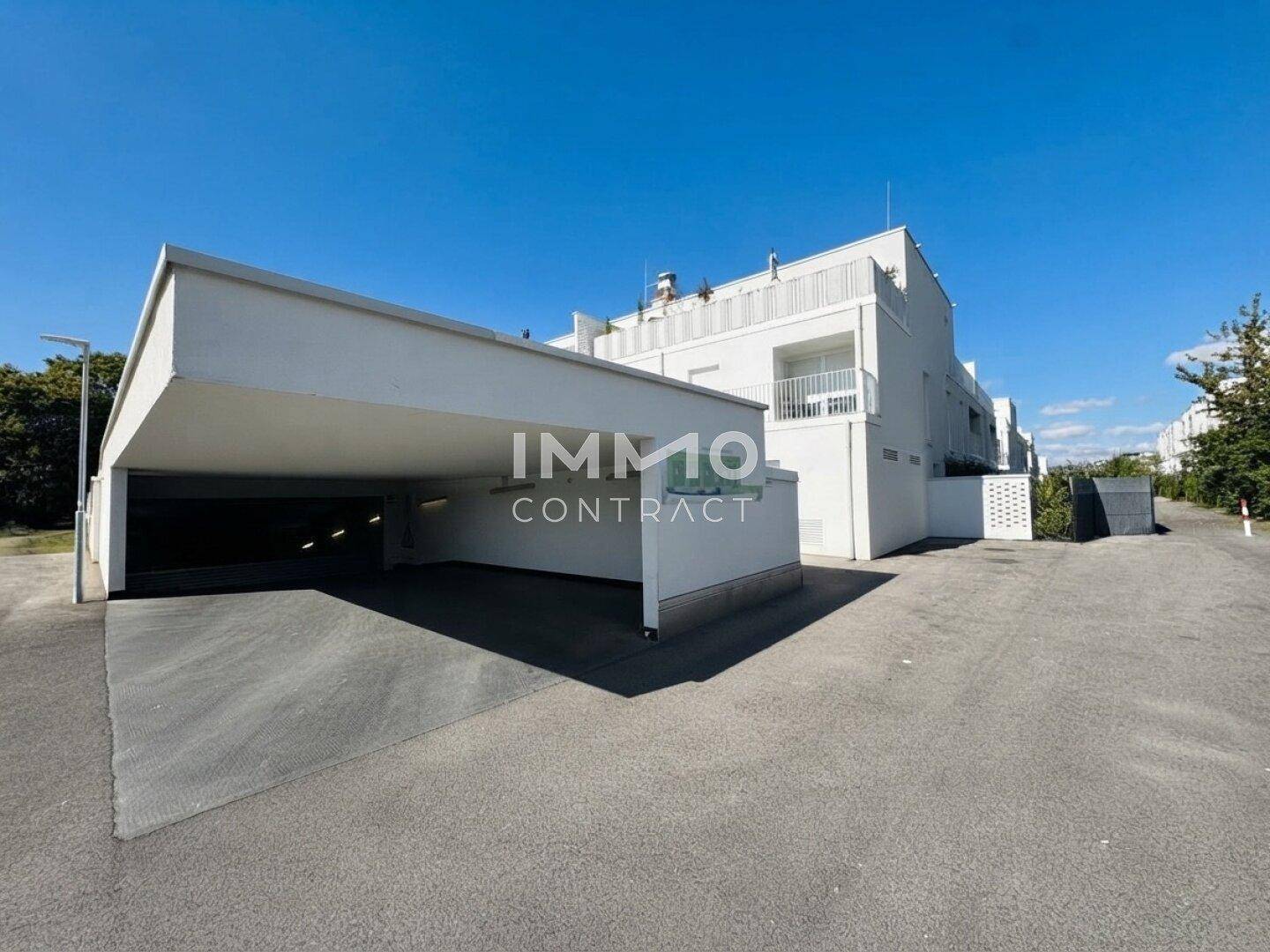 Zufahrt zur Tiefgarage und moderne Fassade der Wohnanlage unter blauem Himmel.