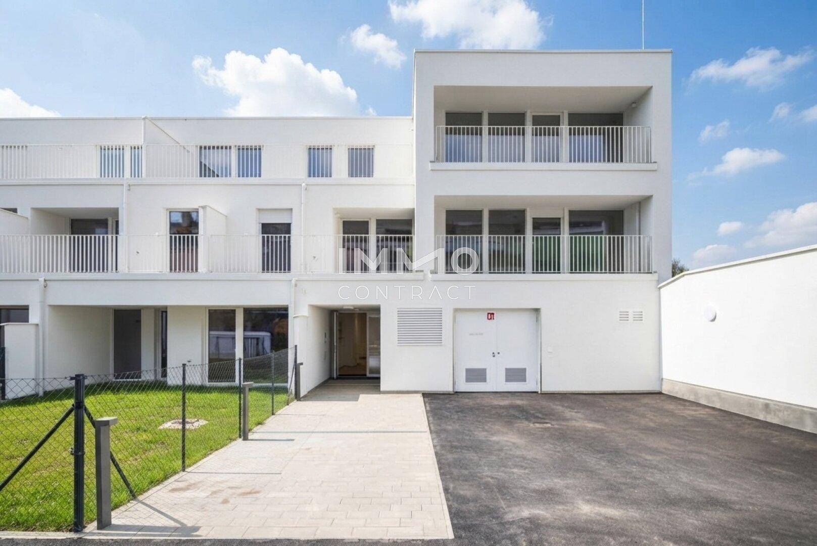 Moderne Wohnanlage mit weißer Fassade, Balkonen und Eingangsbereich.