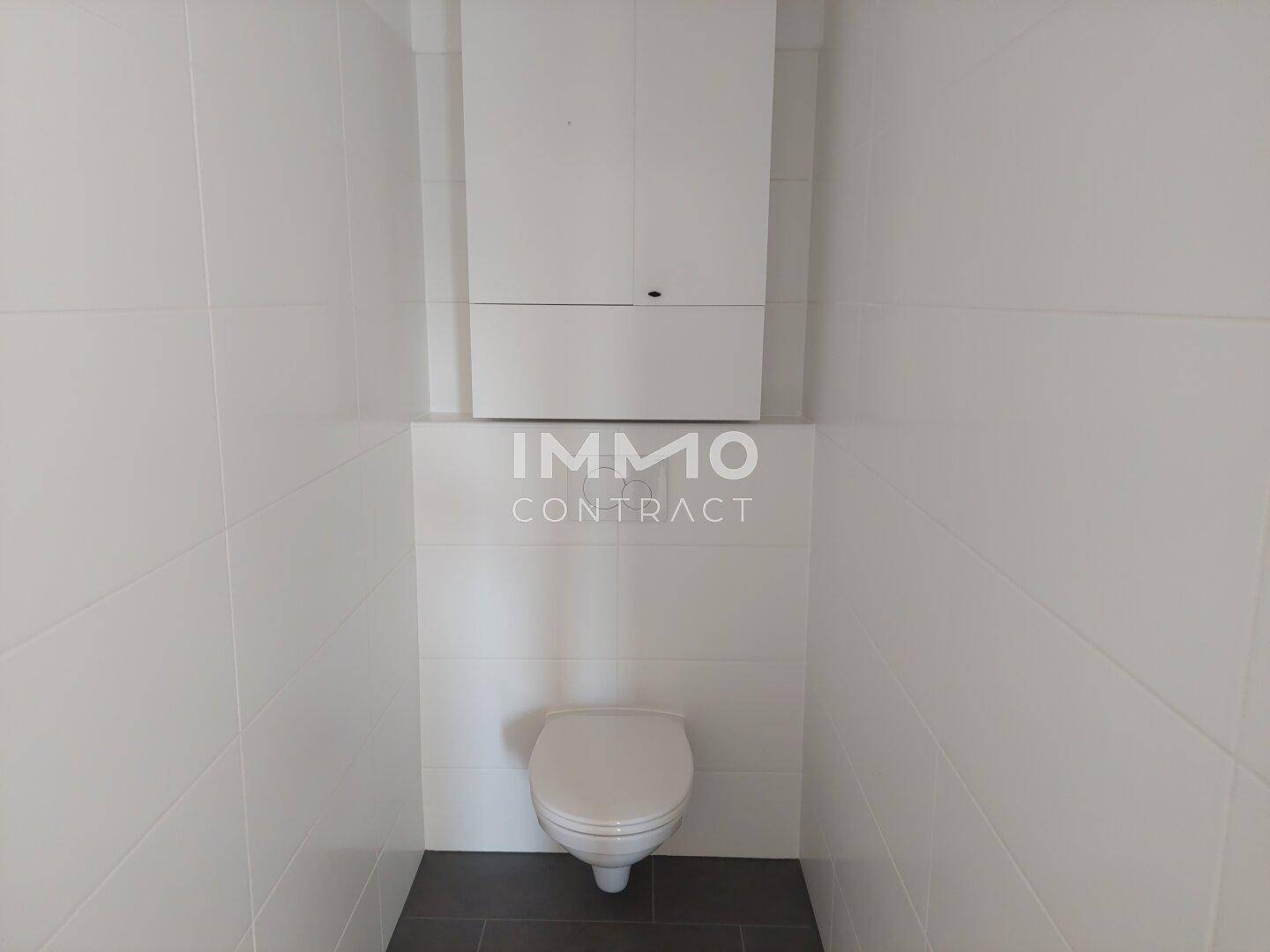 Modern gefliestes WC mit wandhängender Toilette und weißem Spülkasten in minimalistischem Design.