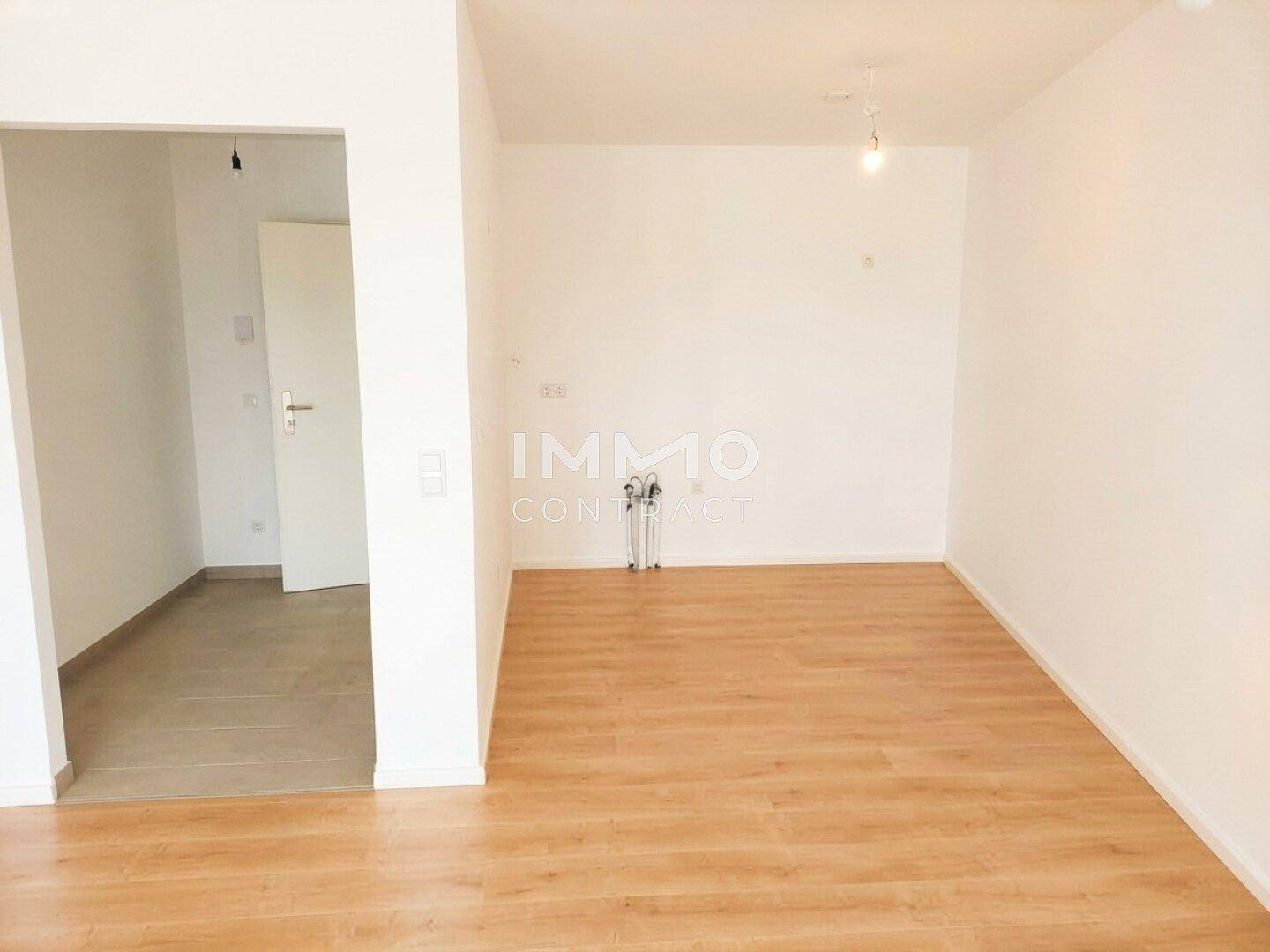 Leerer Flur mit Laminatboden und weiß gestrichenen Wänden, der zu weiteren Räumen führt.