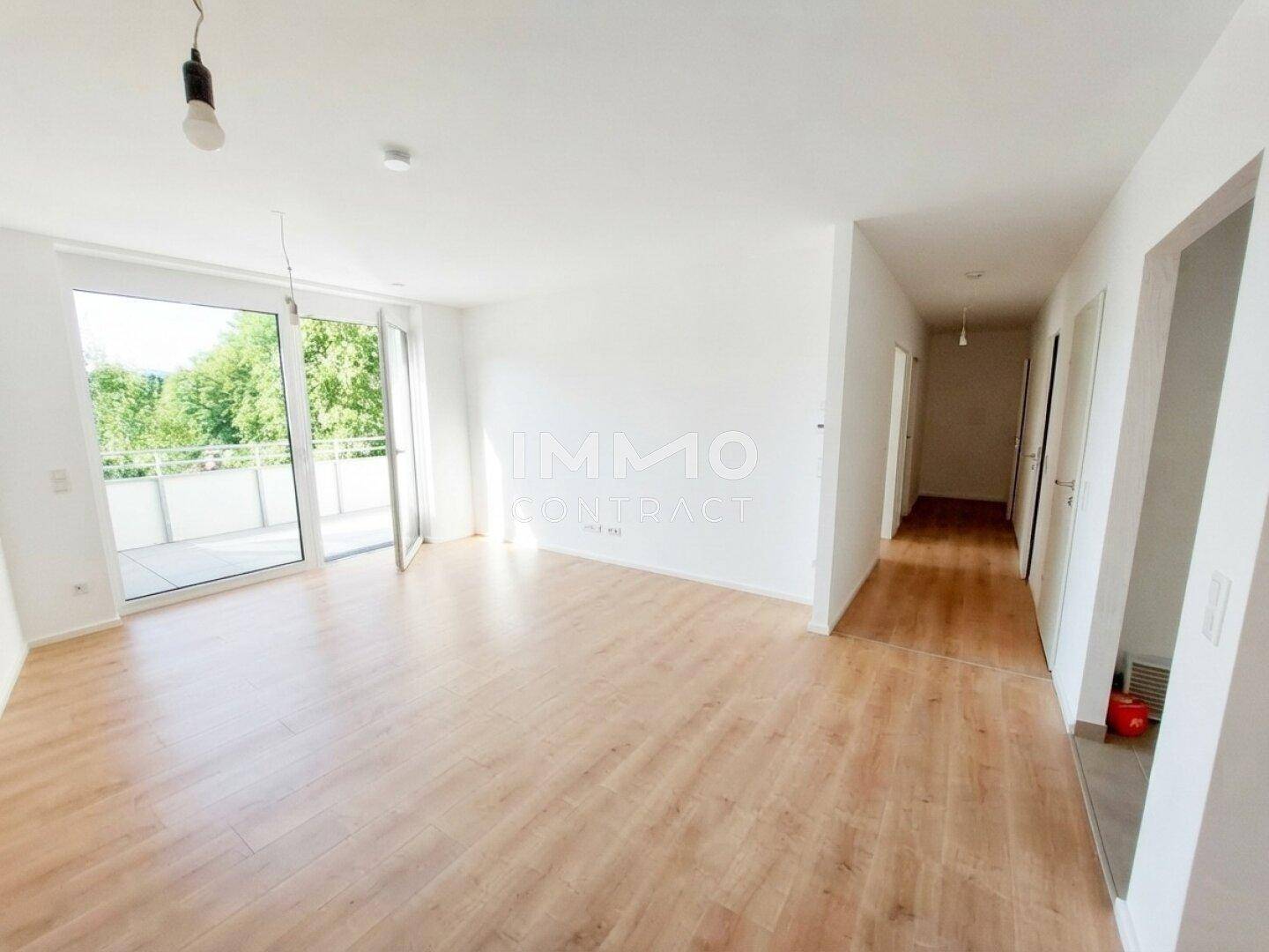 Geräumiger, heller Wohnbereich mit Laminatboden und Zugang zu einem Balkon, der eine weite Aussicht bietet.
