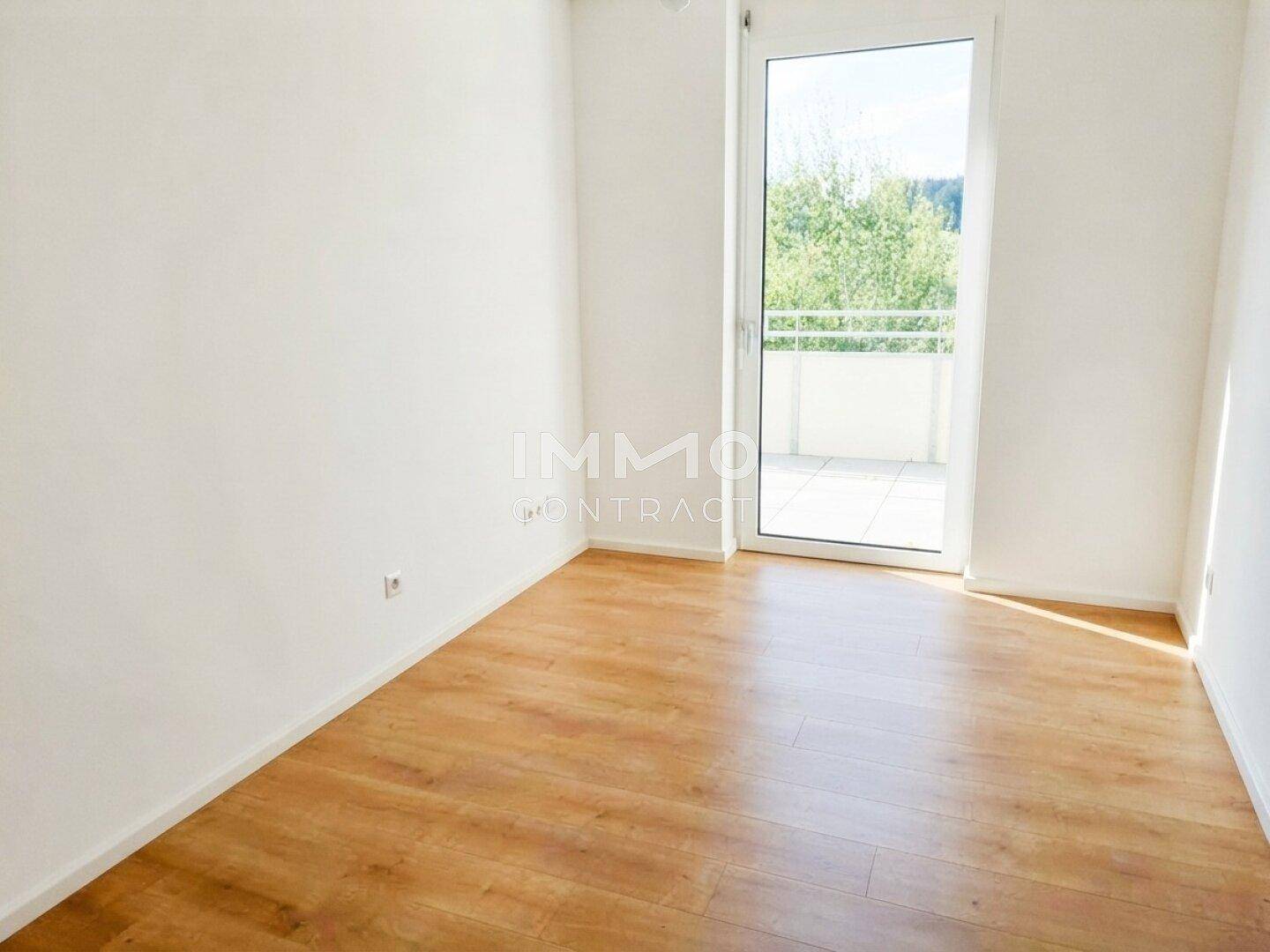 Helles Schlafzimmer mit Laminatboden und direktem Zugang zu einem sonnigen Balkon mit Aussicht.