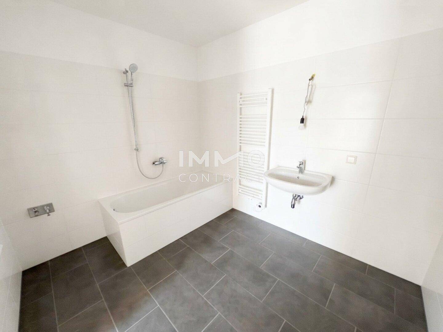 Modernes Badezimmer mit Badewanne, Waschbecken, Handtuchheizkörper und dunklen Bodenfliesen.