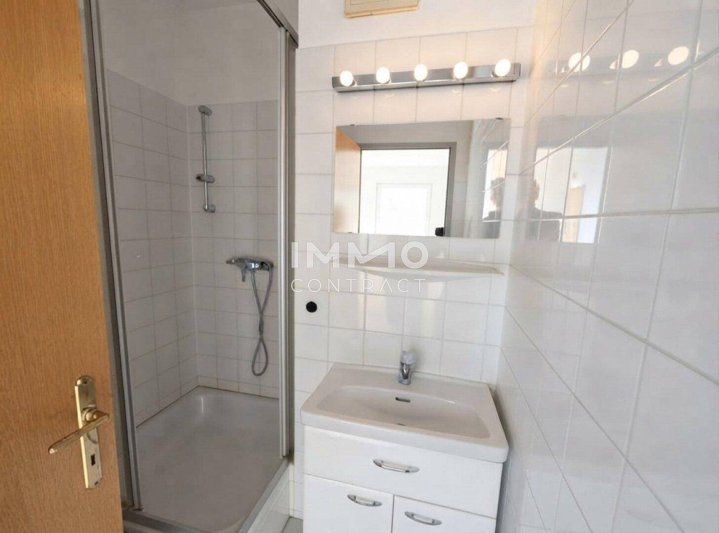 Badezimmer mit weißen Fliesen, Duschkabine und einem Waschbecken mit Spiegelschrank.