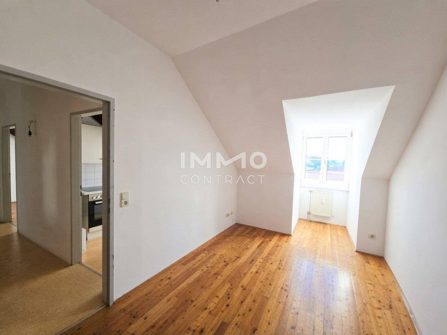 Leerer Raum mit Holzboden, weißen Wänden, Dachschrägen und einem Fenster.