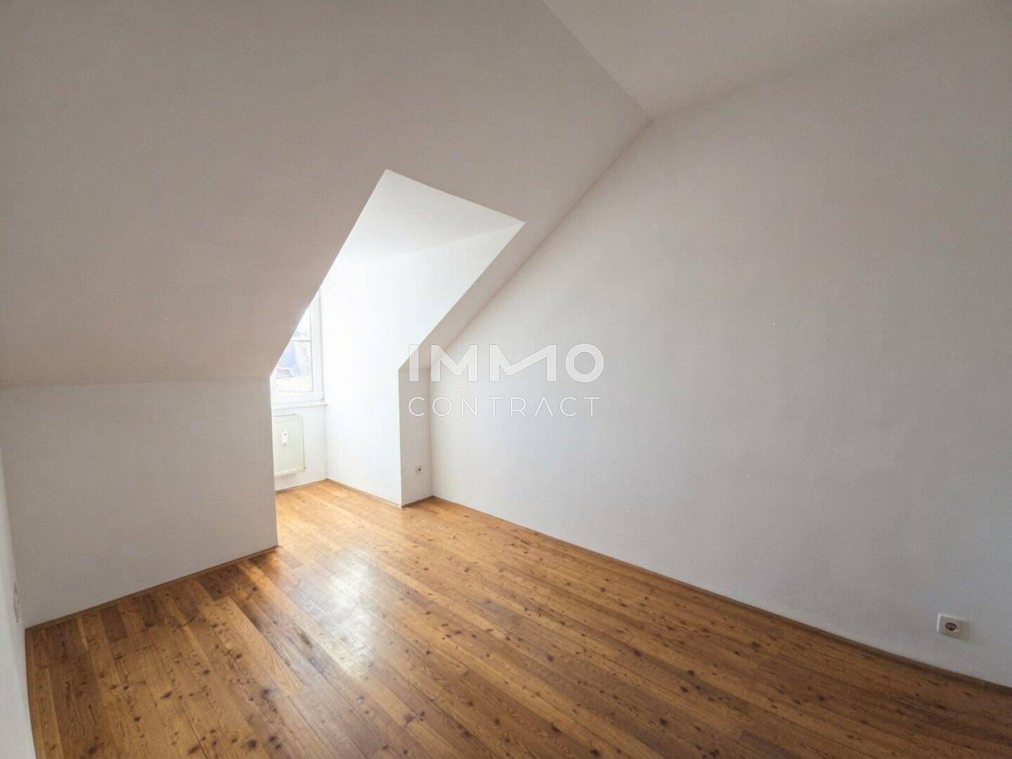 Heller Raum im Dachgeschoss mit Holzdielenboden und schrägen Wänden.
