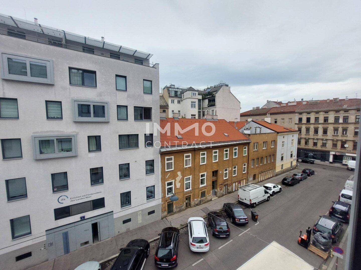 Blick aus dem Fenster auf die Straße mit parkenden Autos und umliegenden Gebäuden.