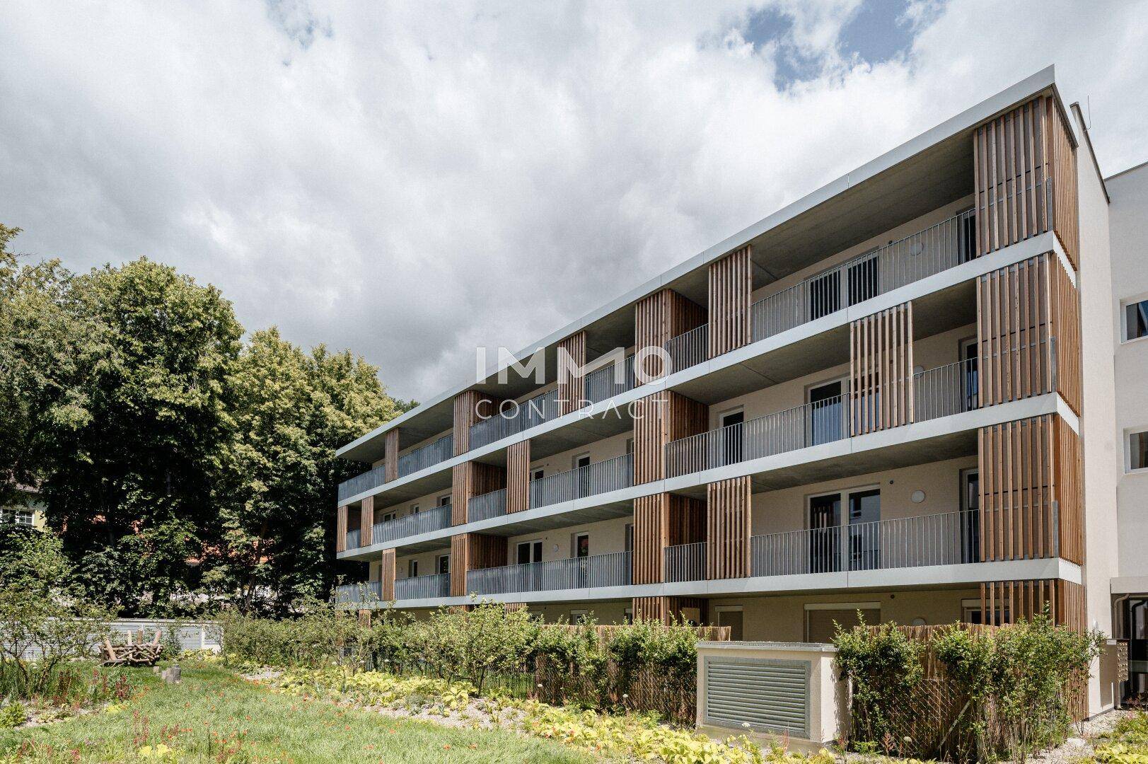 Moderne Gebäudefassade mit Balkonen, die durch vertikale Holzelemente akzentuiert sind, umgeben von Grünflächen.