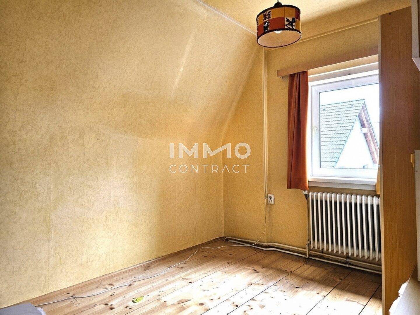 Schlafzimmer im Dachgeschoss mit schrägen Wänden, Holzboden und Fenster.
