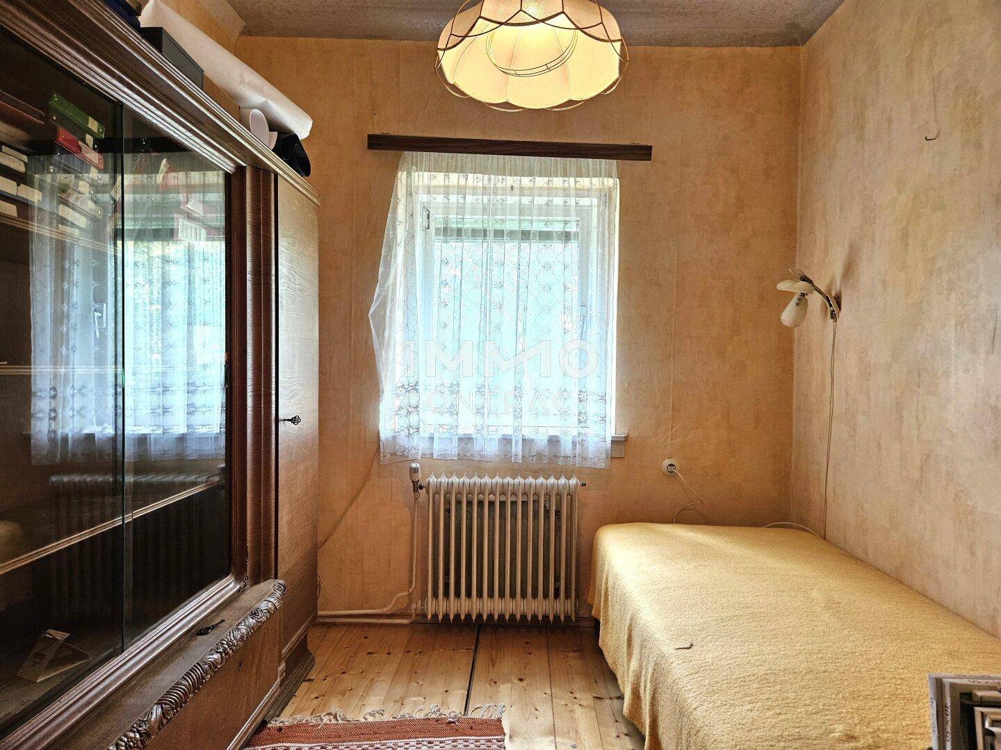 Kleines Schlafzimmer mit Einzelbett, Holzschrank und Fenster, einfacher Stil.
