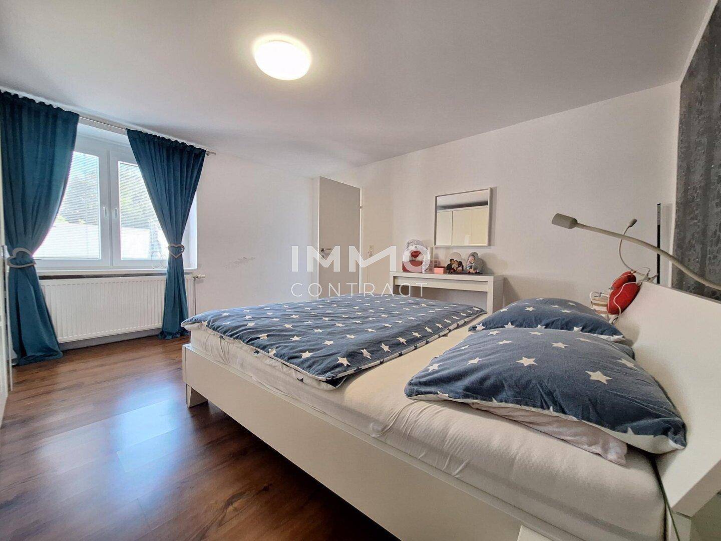 Schlafzimmer mit Holzboden, Doppelbett und blauen Vorhängen an den Fenstern.