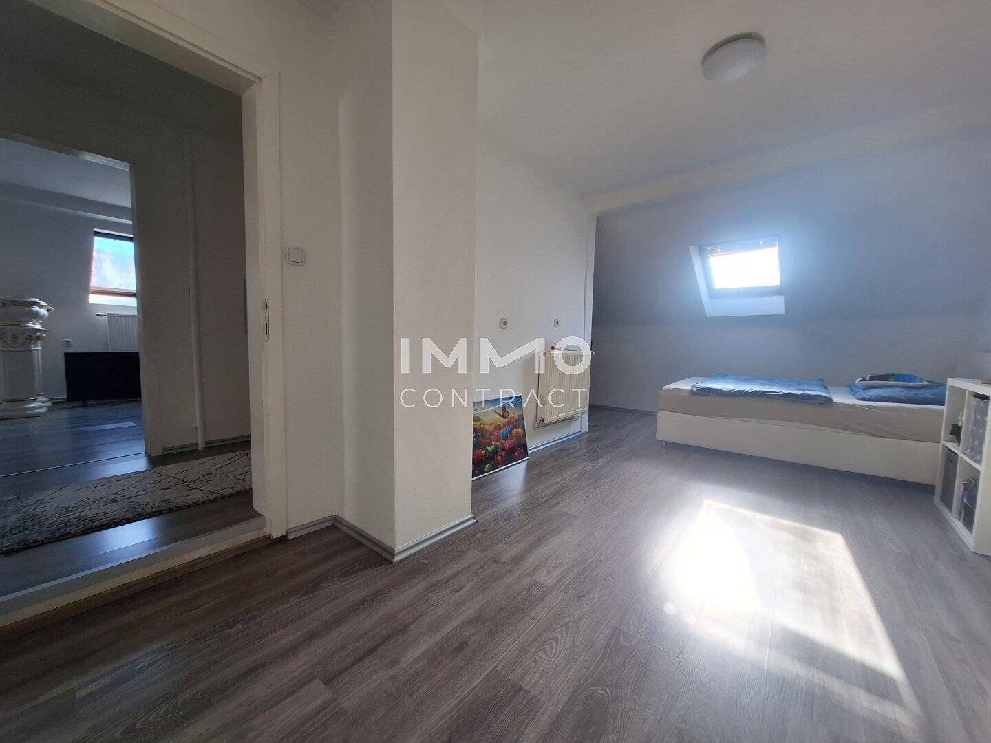Helles Dachgeschoss-Schlafzimmer mit Laminatboden und Dachfenster.