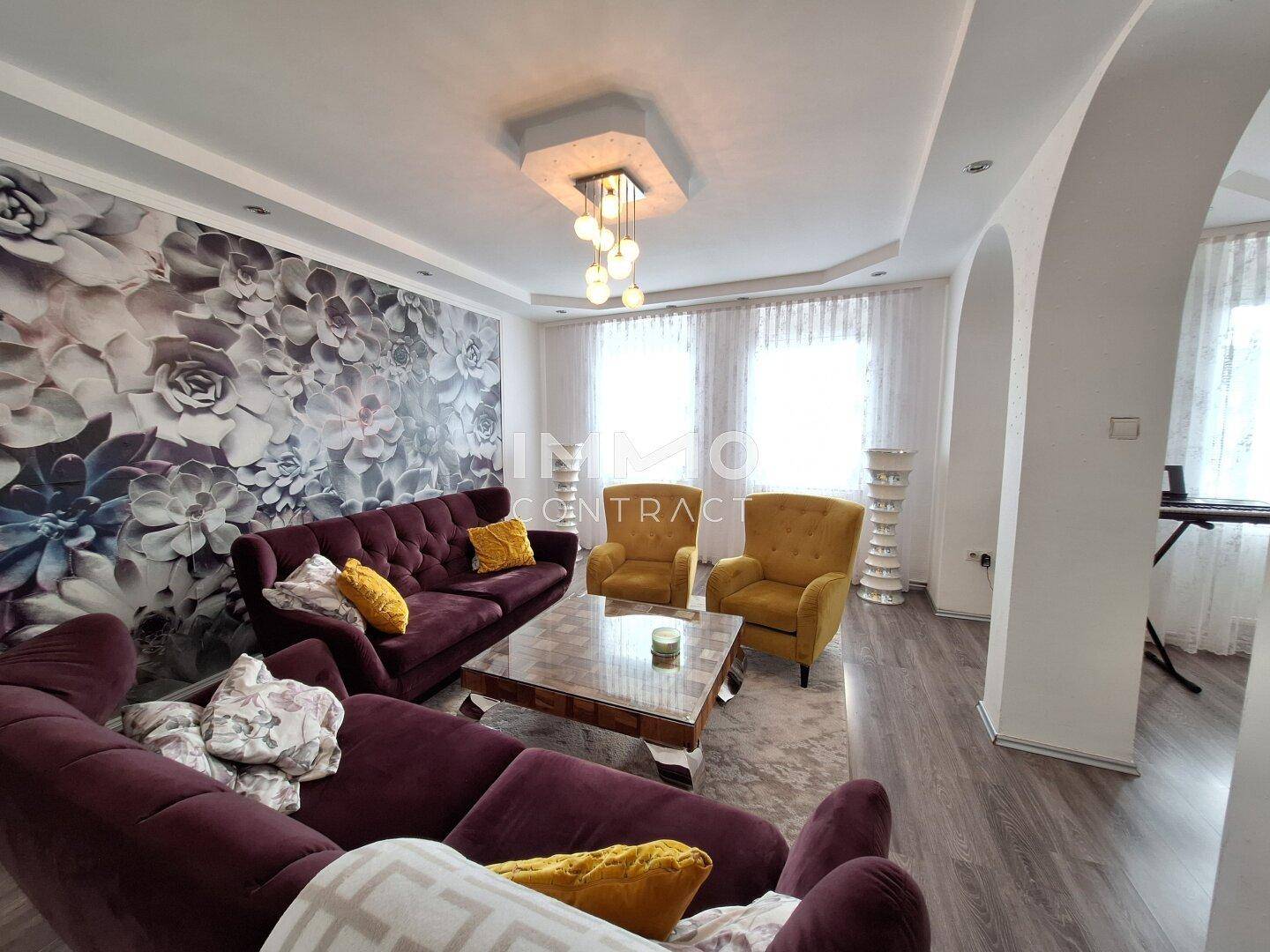 Gemütliches Wohnzimmer mit floraler Tapete, Sofas und gelben Akzentsesseln.