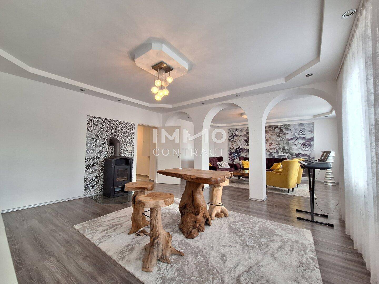 Geräumiges Wohnzimmer mit Holzboden, Kaminofen und dekorativen Bögen.