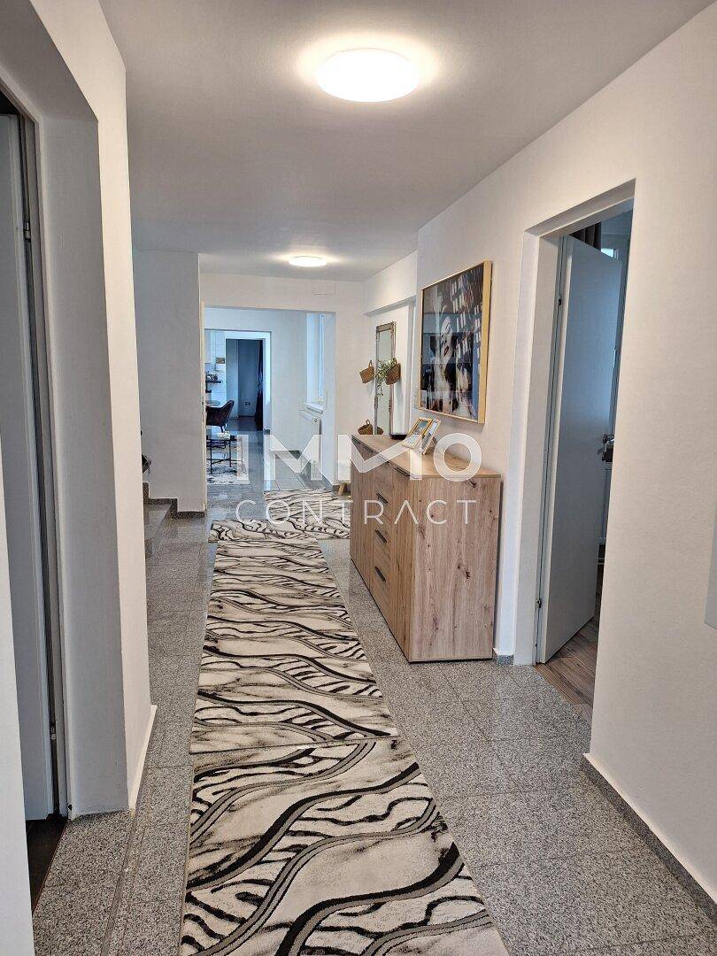 Langer, heller Flur mit Fliesenboden, Teppichläufer und Holzkommode.