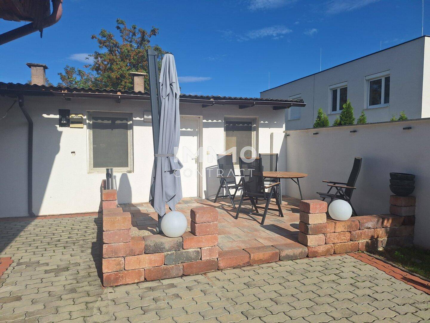 Gepflasterte Terrasse mit Sitzgelegenheiten und Sonnenschirm im Außenbereich.