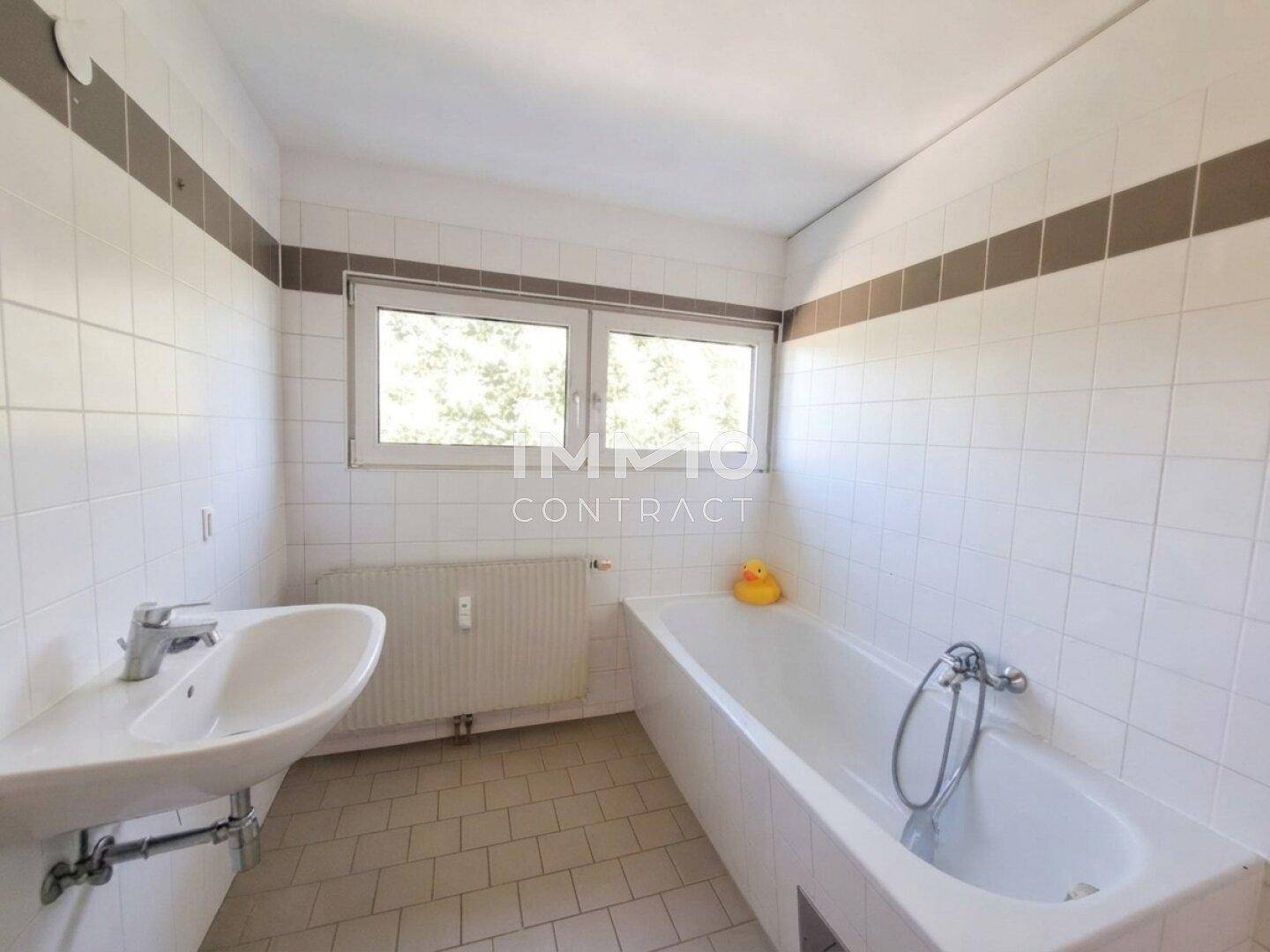 Helles Badezimmer mit weißen Fliesen, Badewanne, Waschbecken und Fenster.