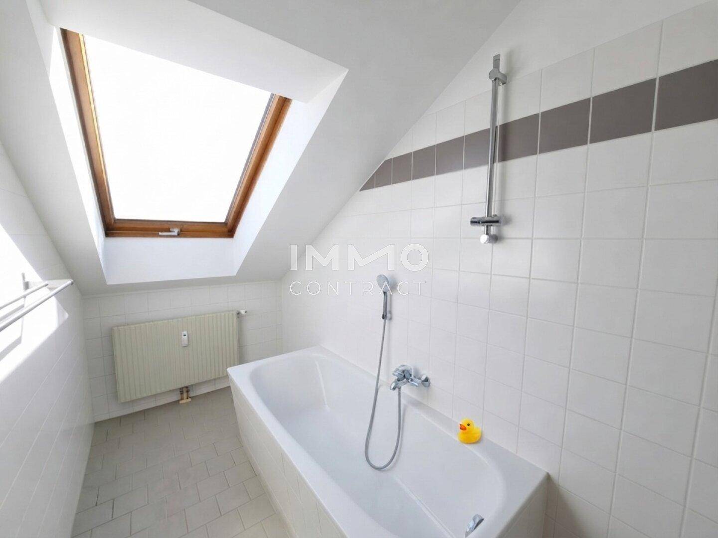 Helles Badezimmer im Dachgeschoss mit Badewanne, Dachfenster und weißen Fliesen.