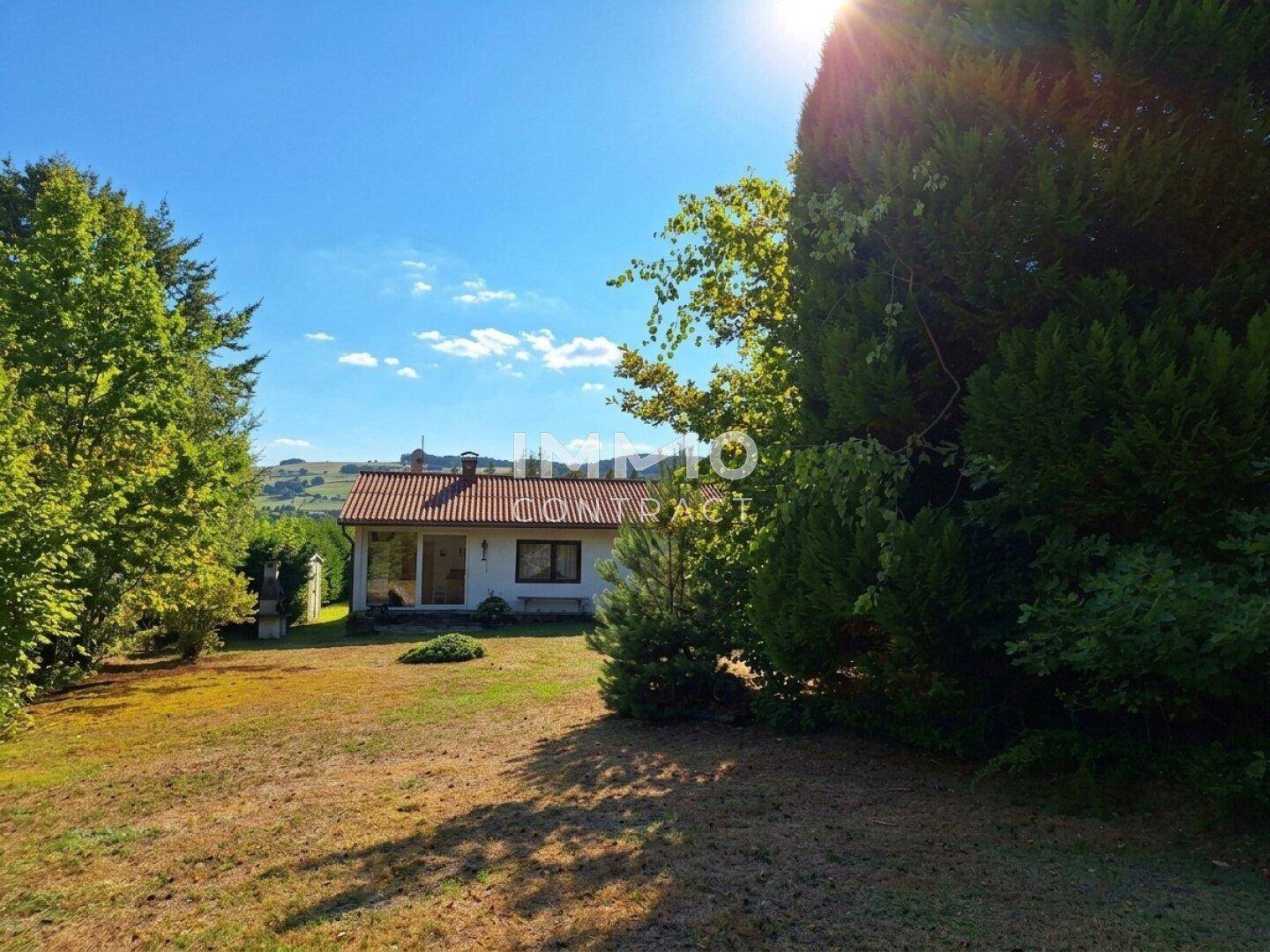 Weitläufiger Gartenbereich mit Einfamilienhaus und Blick auf die umliegende Landschaft an einem sonnigen Tag.