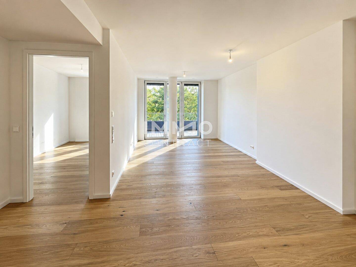 Heller, leerer Wohnraum mit Eichenparkett und Zugang zu einem Balkon oder einer Terrasse.