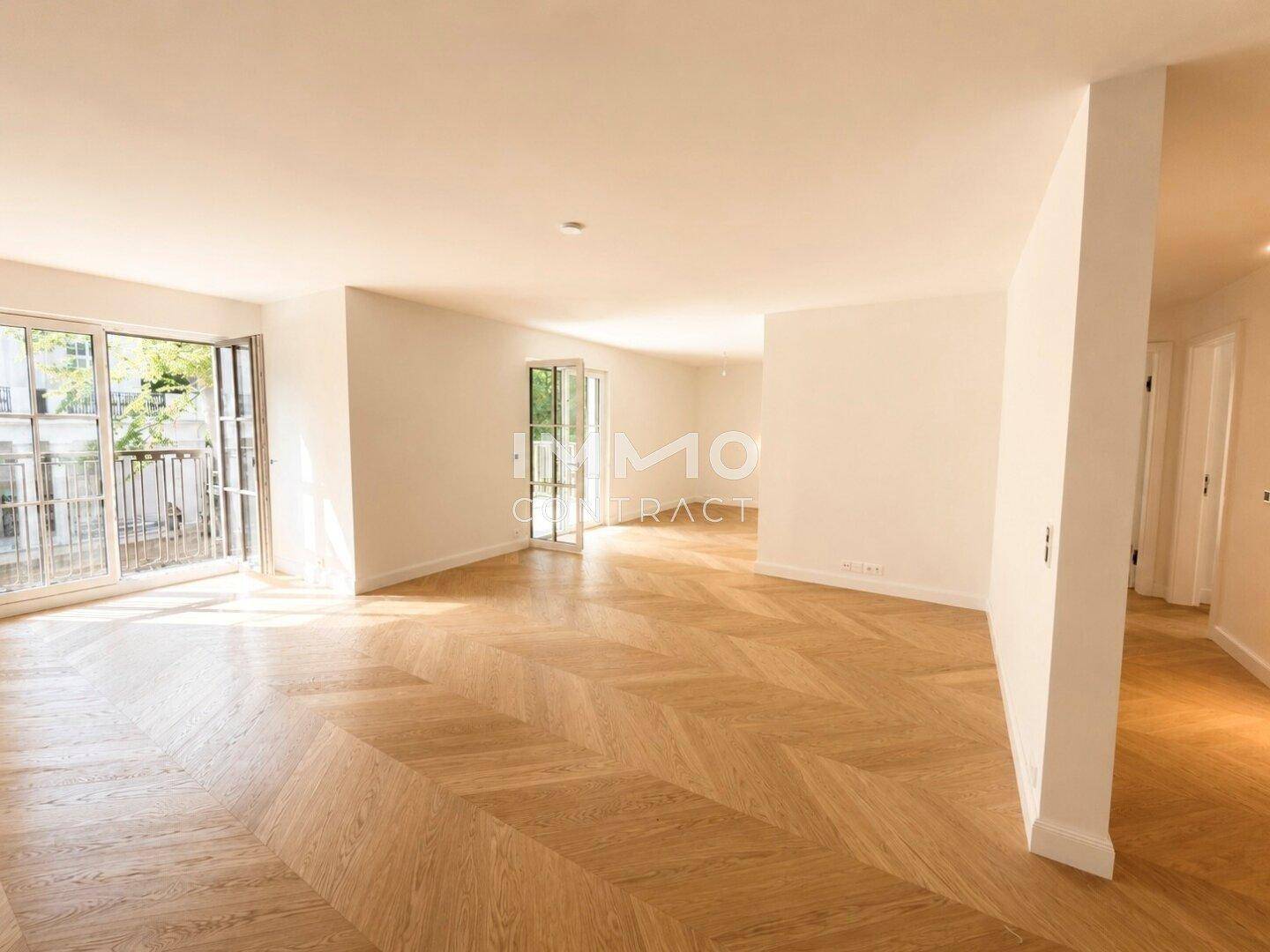 Heller, leerer Wohnbereich mit elegantem Fischgrätparkett und Zugang zu einem französischen Balkon.