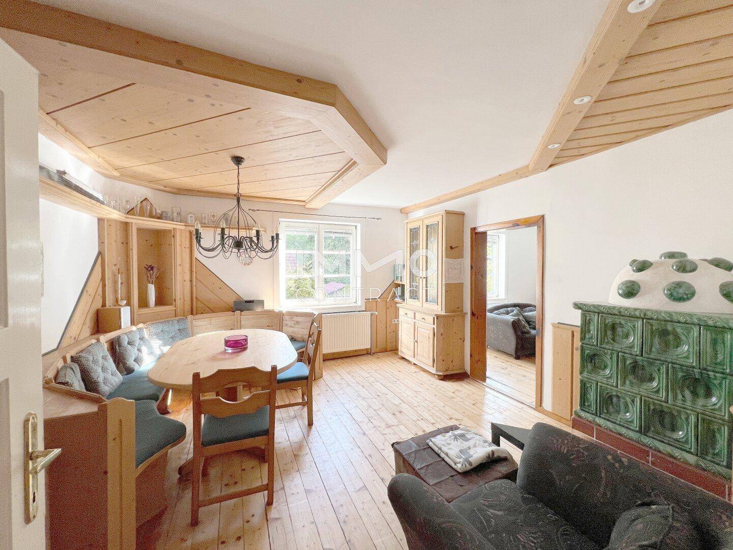 Gemütlicher Wohn-Essbereich im alpinen Stil mit Holzböden, Holzdecken und einem traditionellen Kachelofen.
