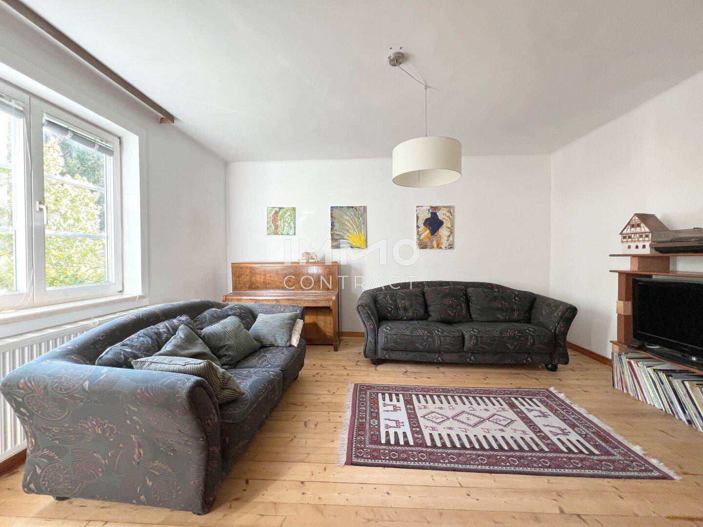 Geräumiges Wohnzimmer mit Holzboden, zwei Sofas, einem Klavier und Blick ins Grüne.