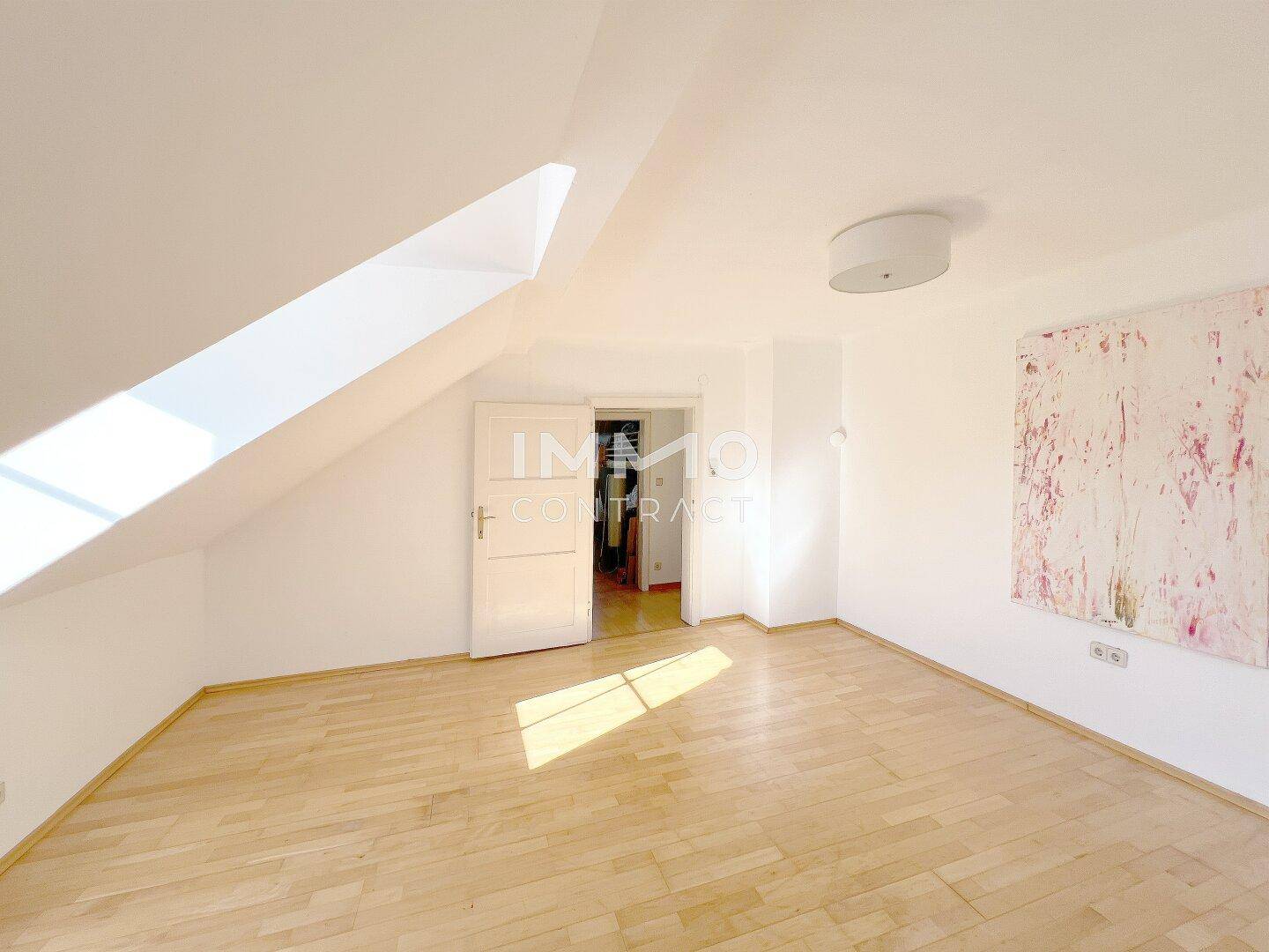 Geräumiges Dachzimmer mit Holzboden, schrägen Wänden und einem Dachfenster für viel Tageslicht.
