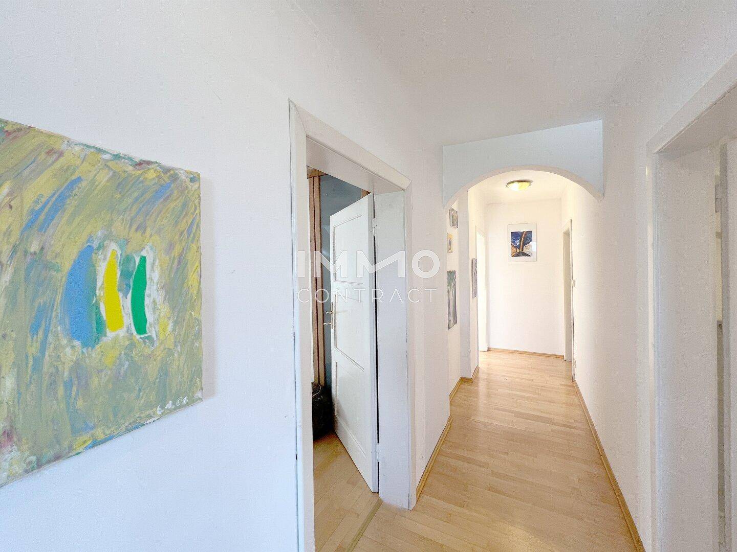 Heller Flur mit Holzboden und weiß gestrichenen Wänden, der zu weiteren Räumen führt.