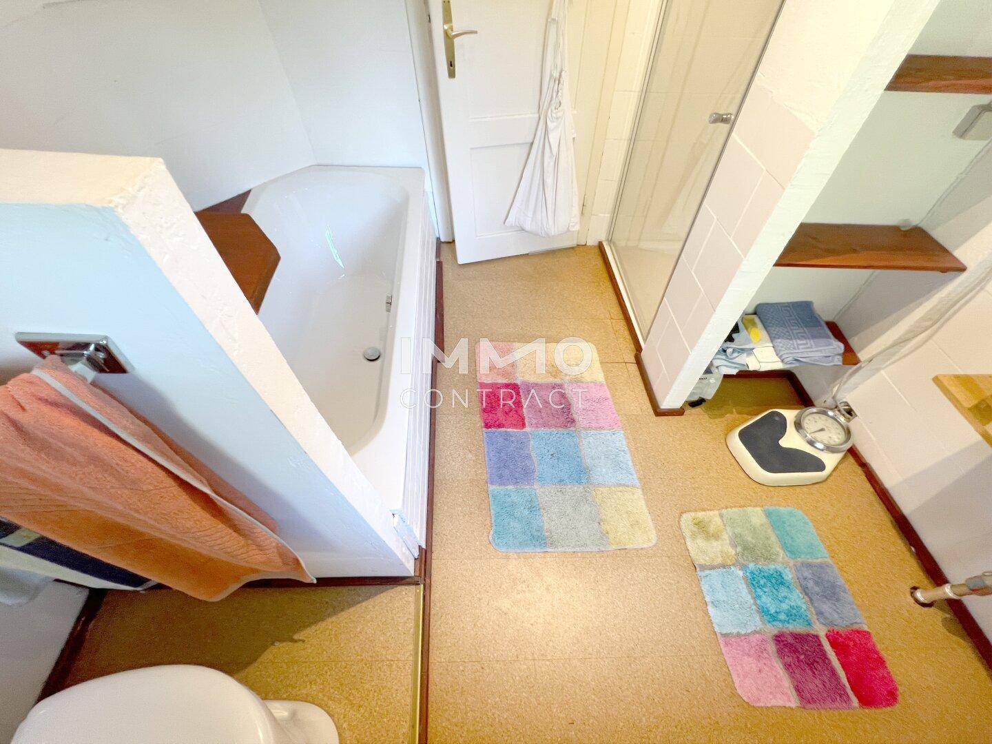 Funktionales Badezimmer mit Badewanne, Duschkabine und bunten Badematten auf dem Boden.