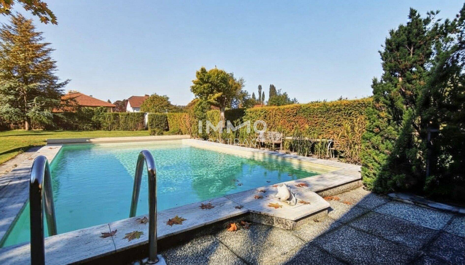 Großer Außenpool umgeben von einer gepflasterten Terrasse und einer dichten Hecke.