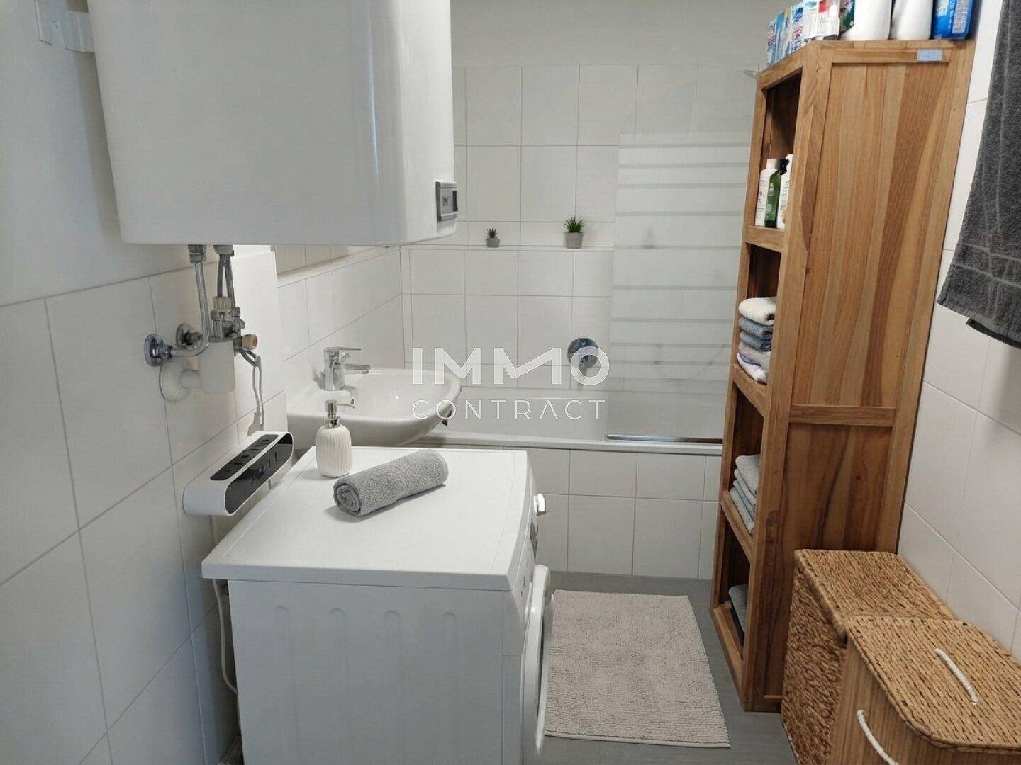 Helles Badezimmer mit Badewanne, Waschbecken und Waschmaschine, ausgestattet mit weißen Fliesen.