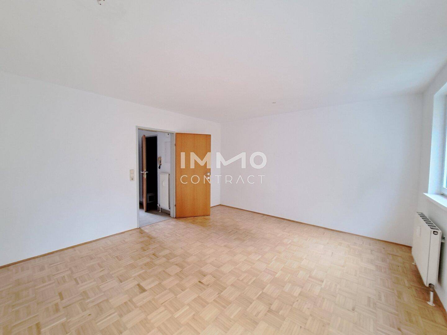 Geräumiges, leeres Zimmer mit Parkettboden und Zugang zu einem weiteren Raum.