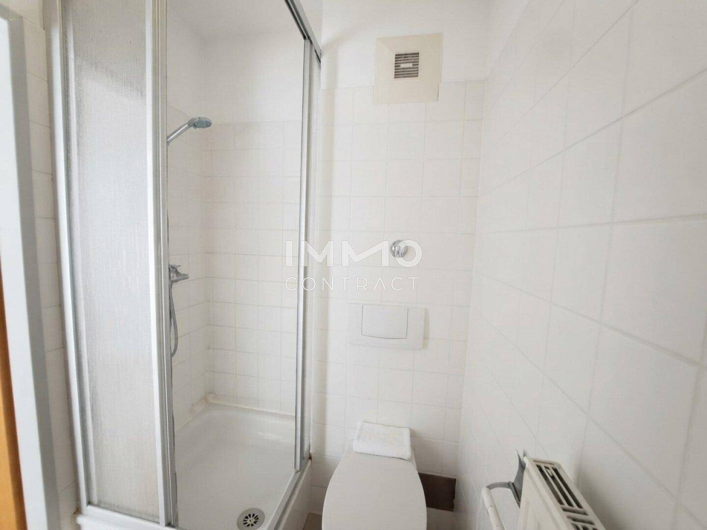 Helles Badezimmer mit Duschkabine, Toilette und Heizkörper, komplett gefliest.