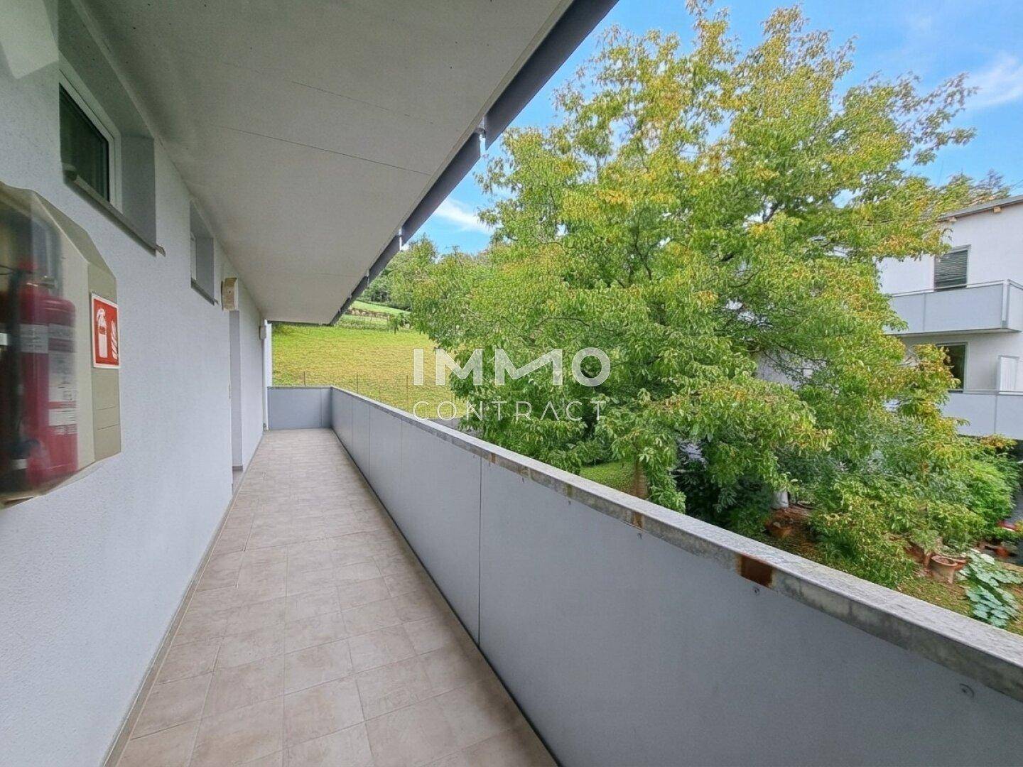 Langer Balkon mit Fliesenboden und Blick auf Bäume und eine grüne Wiese.