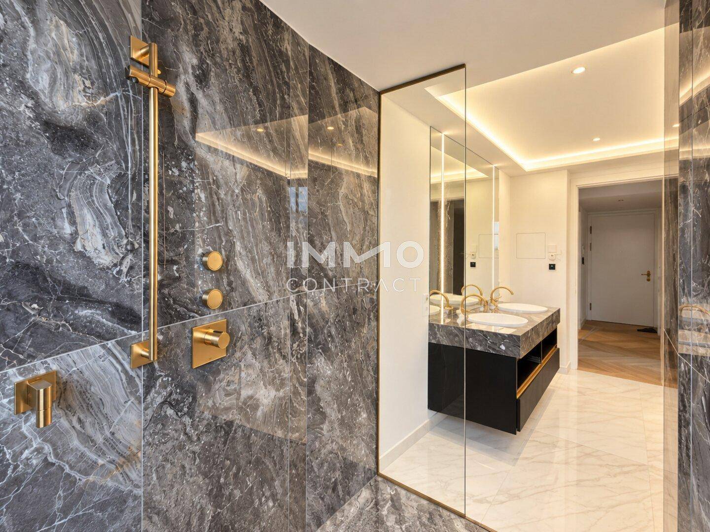 Luxuriöses Badezimmer mit dunklen Marmorfliesen, goldenen Armaturen und Doppelwaschbecken.