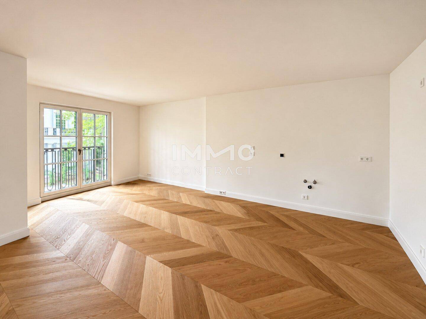 Großzügiger Raum mit elegantem Fischgrätparkett und einem französischen Balkon, ideal für Wohnen.
