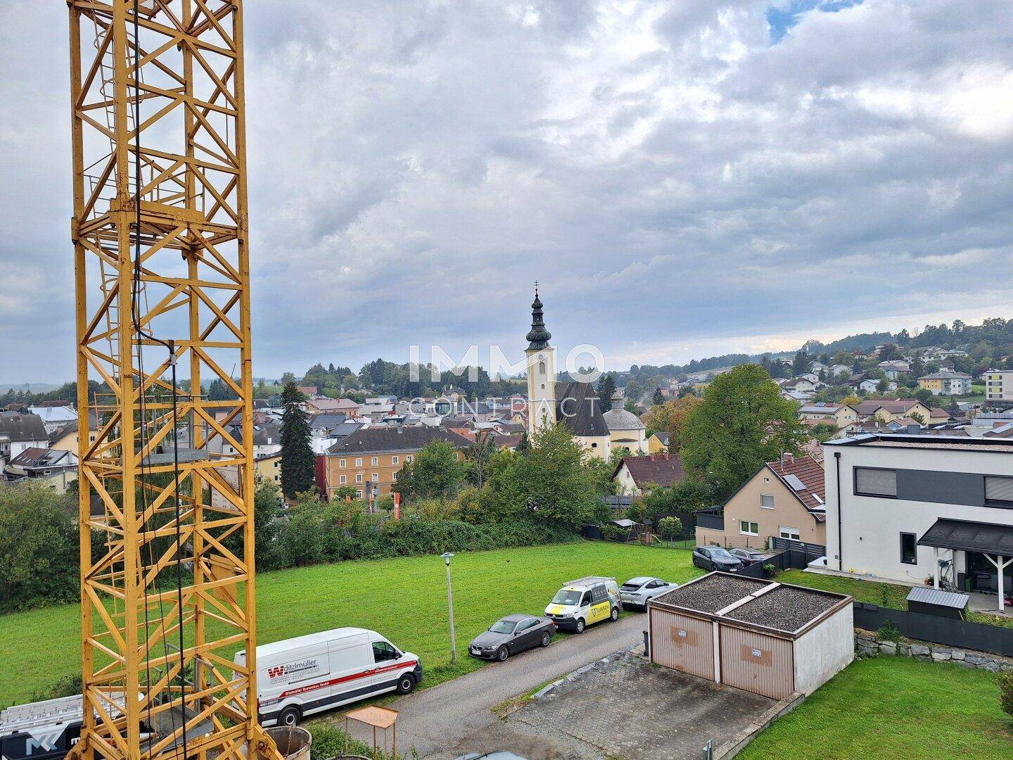 Panoramablick über eine ländliche Ortschaft mit Kirchturm, Wohnhäusern und viel Grün.