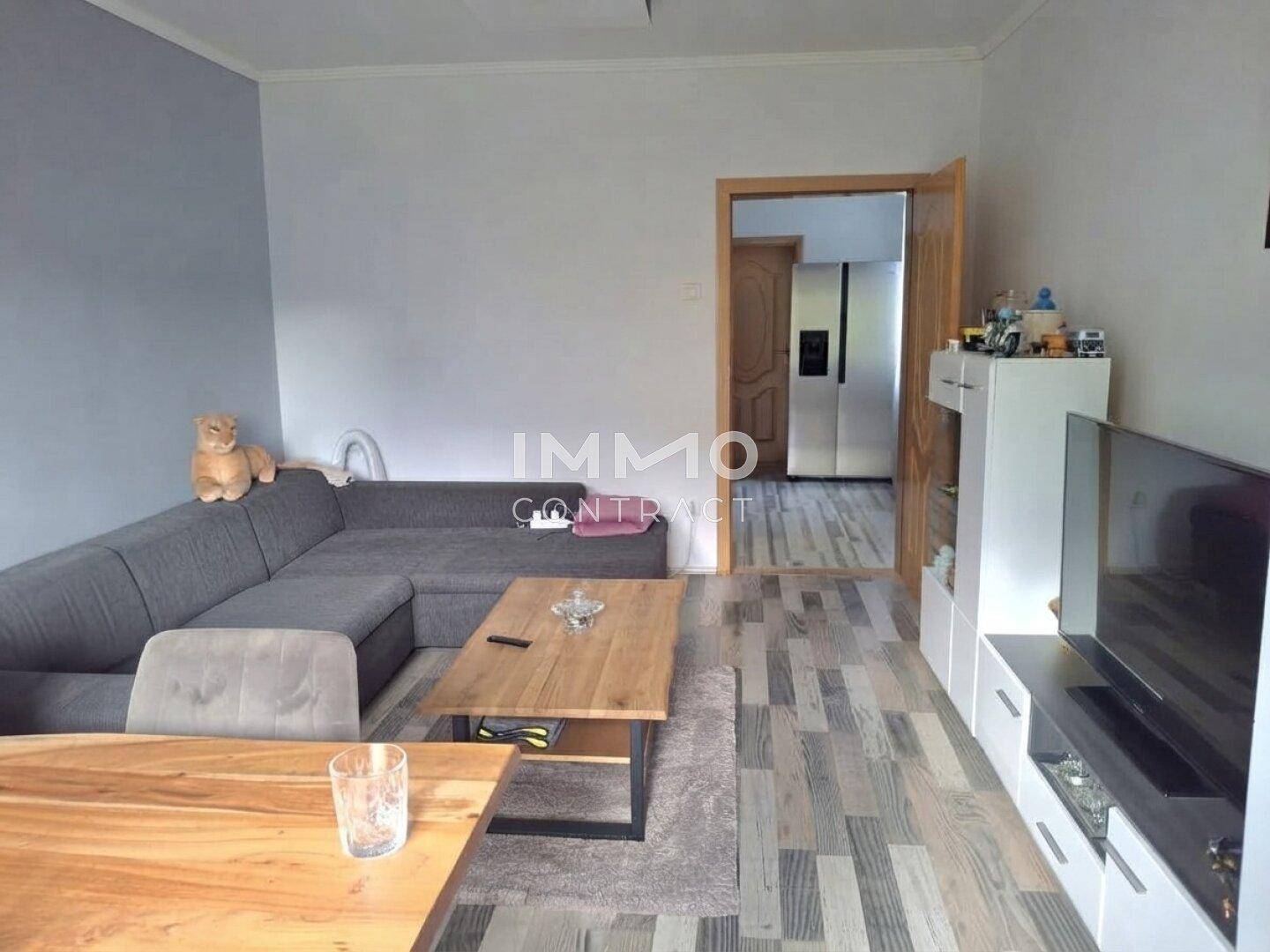 Gemütliches Wohnzimmer mit grauem Ecksofa, Holztisch und Laminatboden.