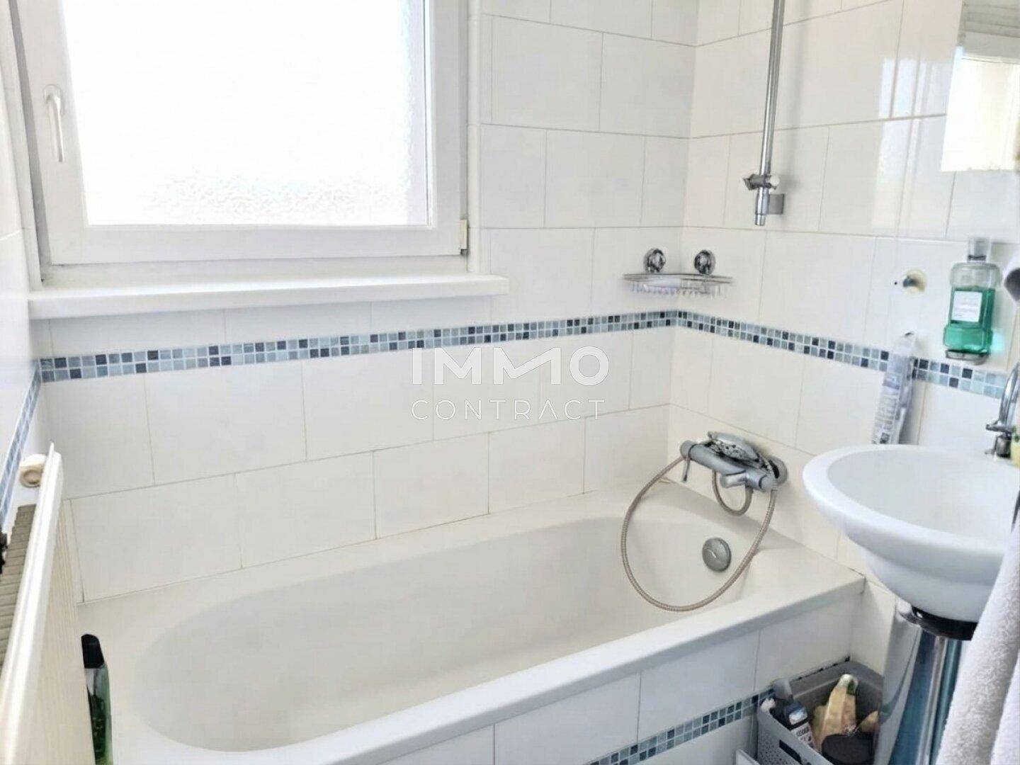 Helles Badezimmer mit Badewanne, Duschfunktion, Waschbecken und Fenster.