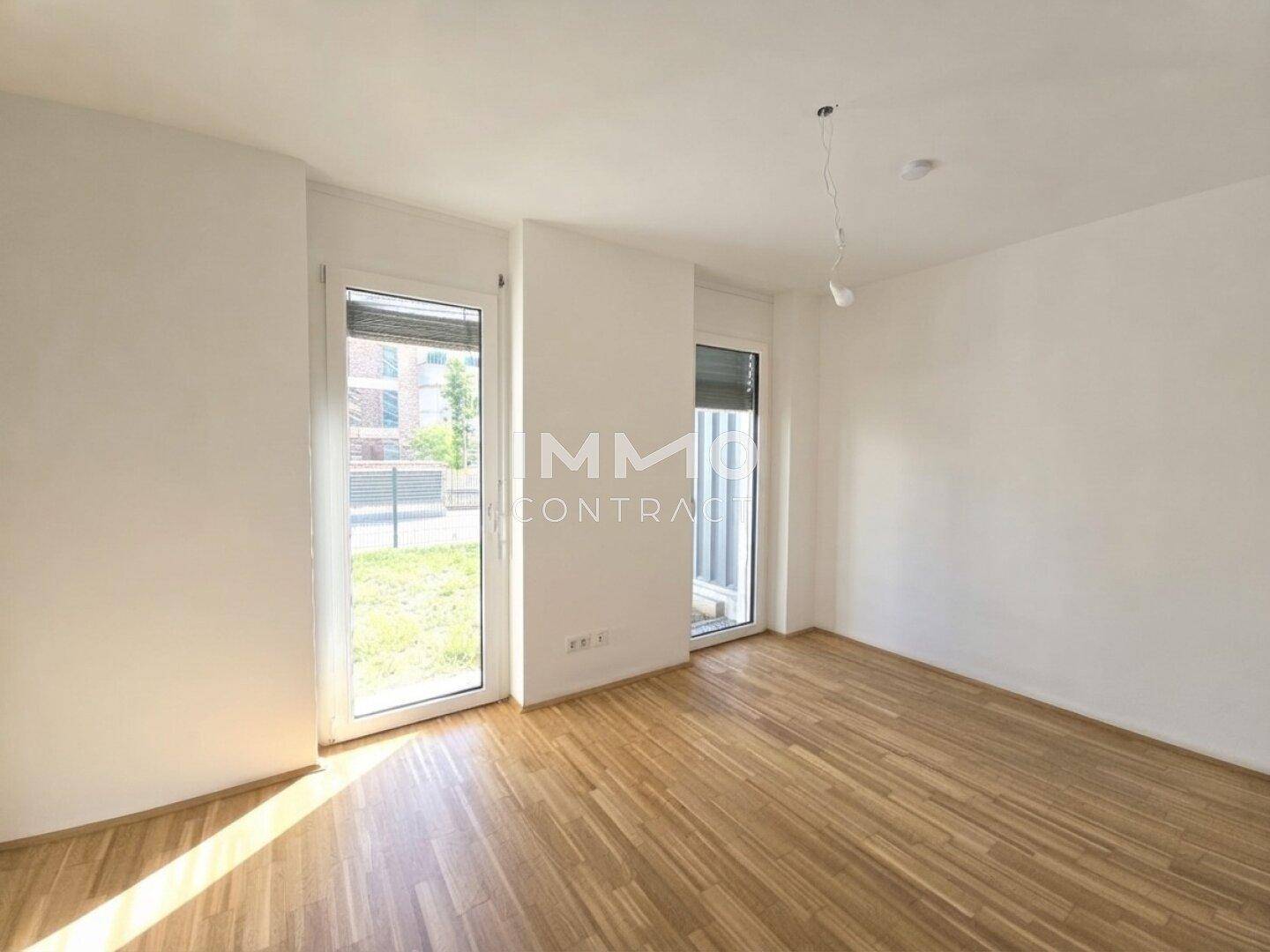 Unmöbliertes Zimmer mit hellem Holzboden und großen Fenstern für viel Tageslicht.