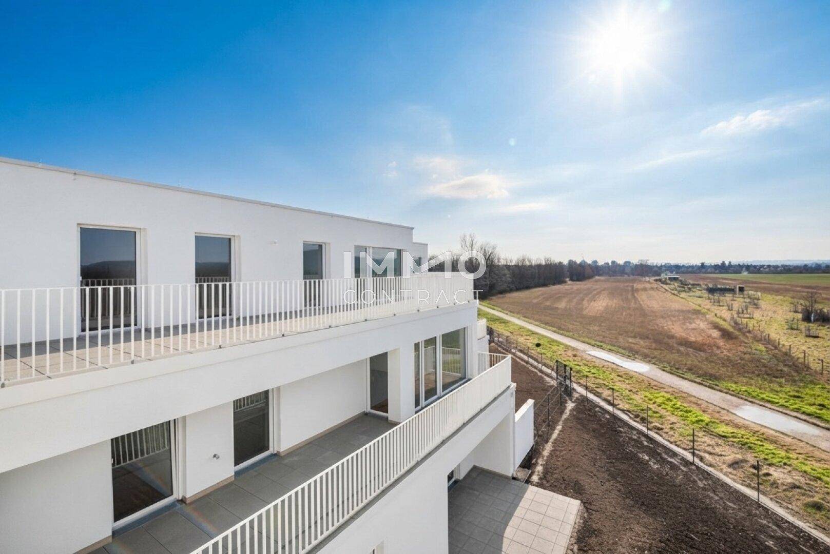 Sonniger Balkon mit weitem Blick über grüne Felder und die umliegende Landschaft.