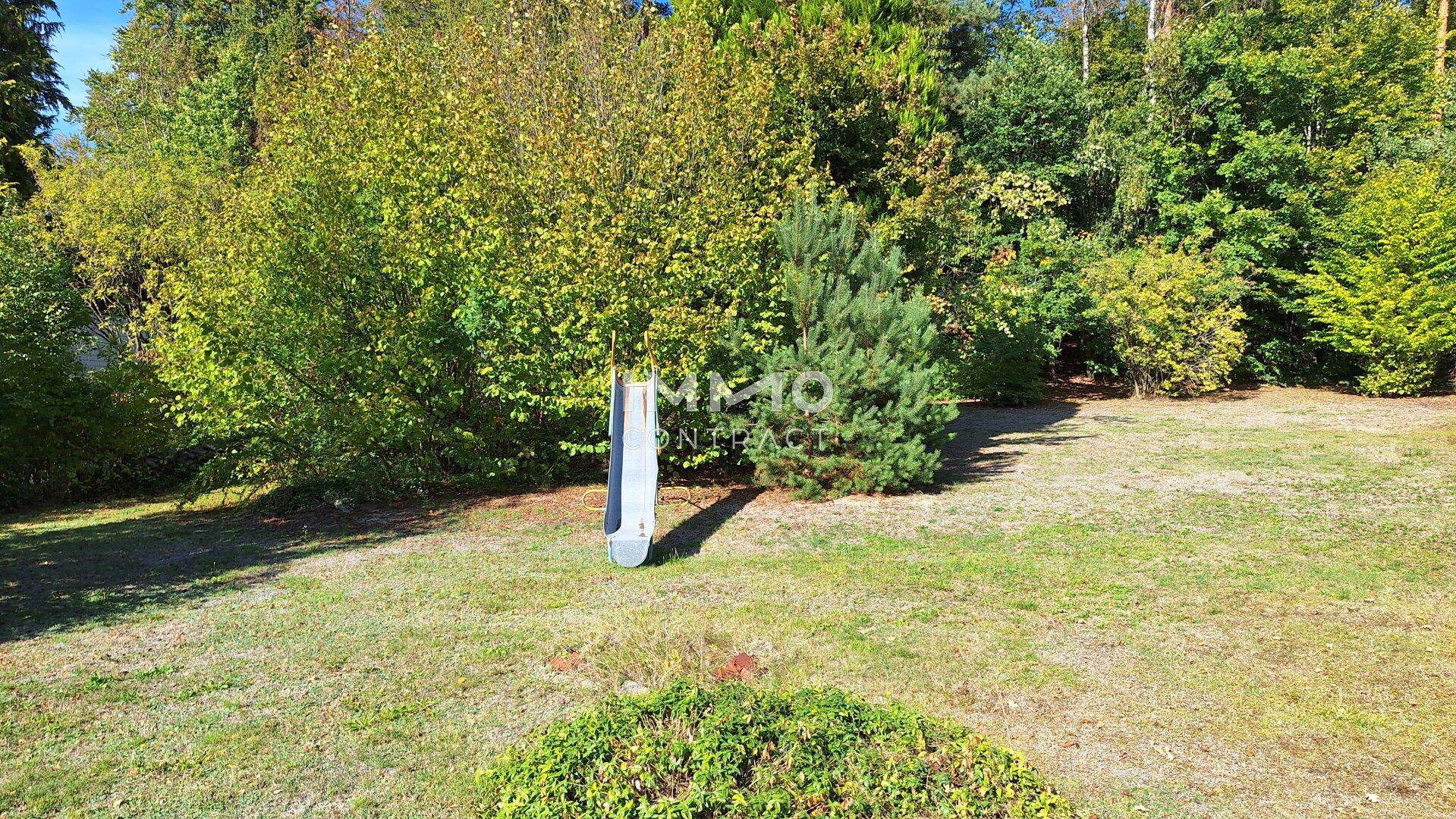 Weitläufiger Gartenbereich mit Rasenfläche, Bäumen und einer kleinen Kinderrutsche.