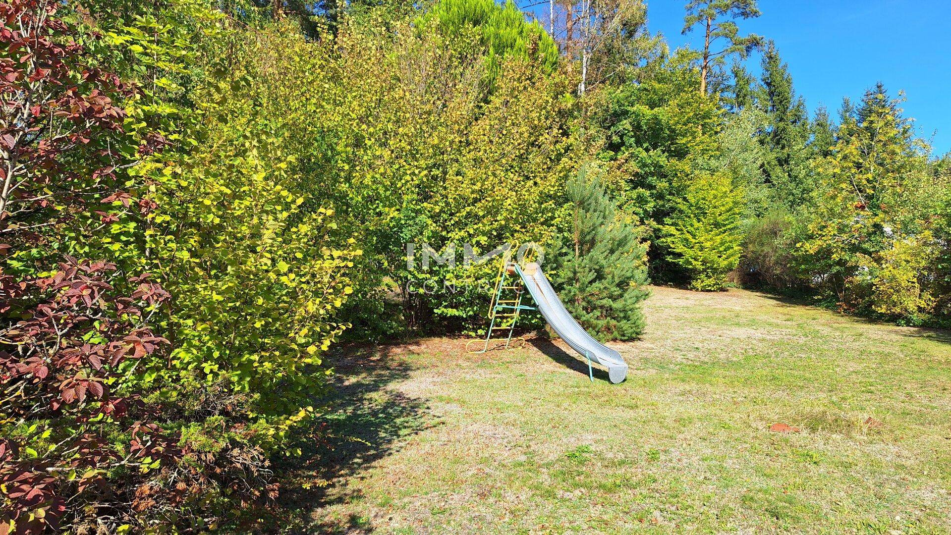 Detailansicht des Gartens mit Rasen, üppiger Vegetation und einer Kinderrutsche.